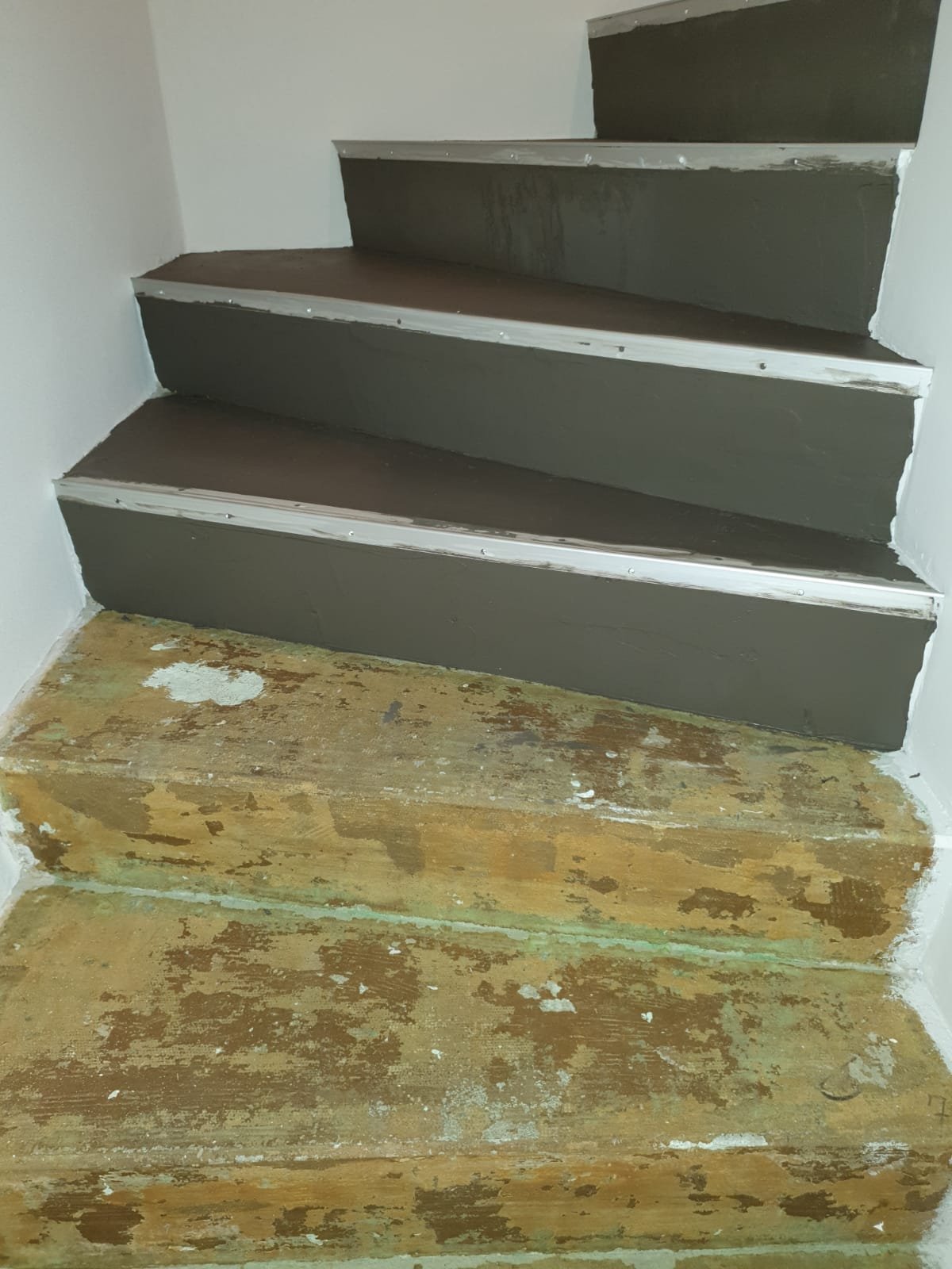 Innenseite einer Treppe mit vier Stufen, die obere zwei sind neu gestrichen, die untere sind abgenutzt und alt. Das Holz der unteren Stufe ist sichtbar und stark abgenutzt.