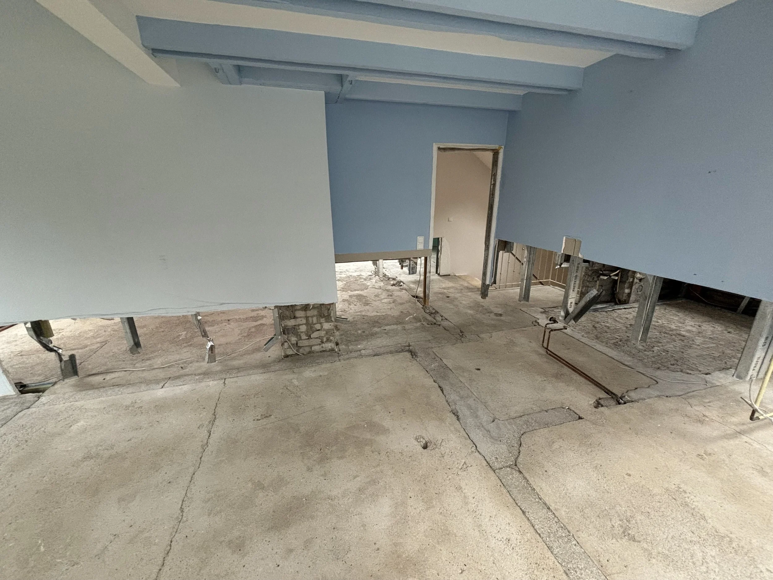 Bauarbeiten im Innenbereich eines Gebäudes, mit offener Bodenplatte, sichtbaren Wänden und Rohren.