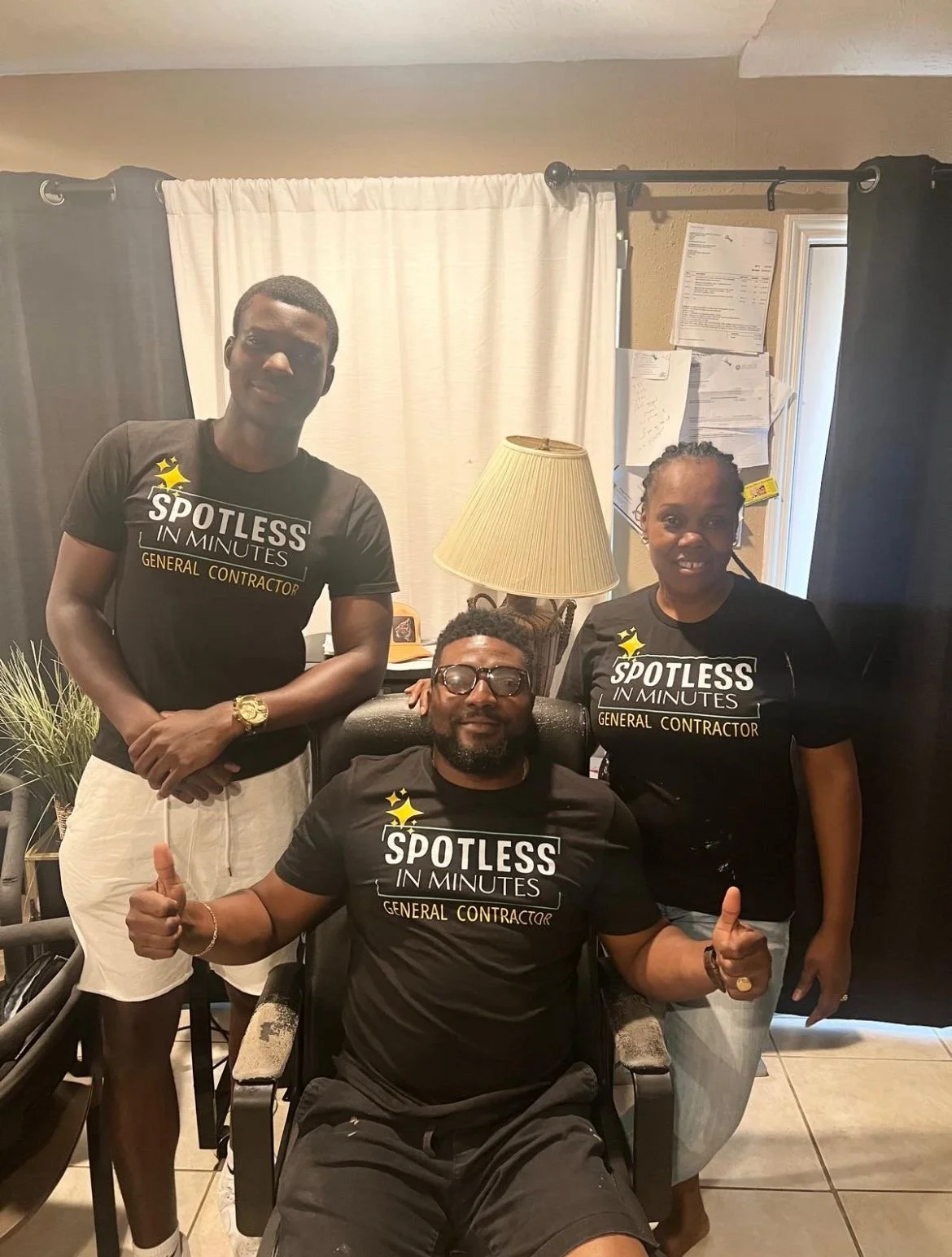 Three people wearing "Spotless in Minutes" general contractor T-shirts, two standing and one sitting with thumbs up, in an office setting.