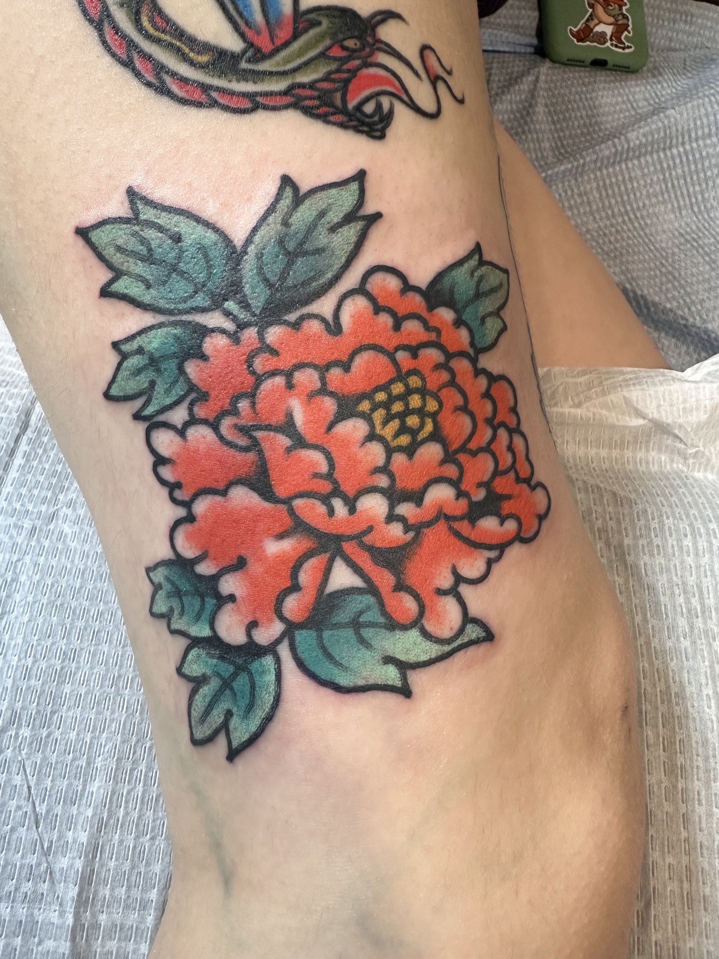 Tattoo of a red flower with green leaves on skin