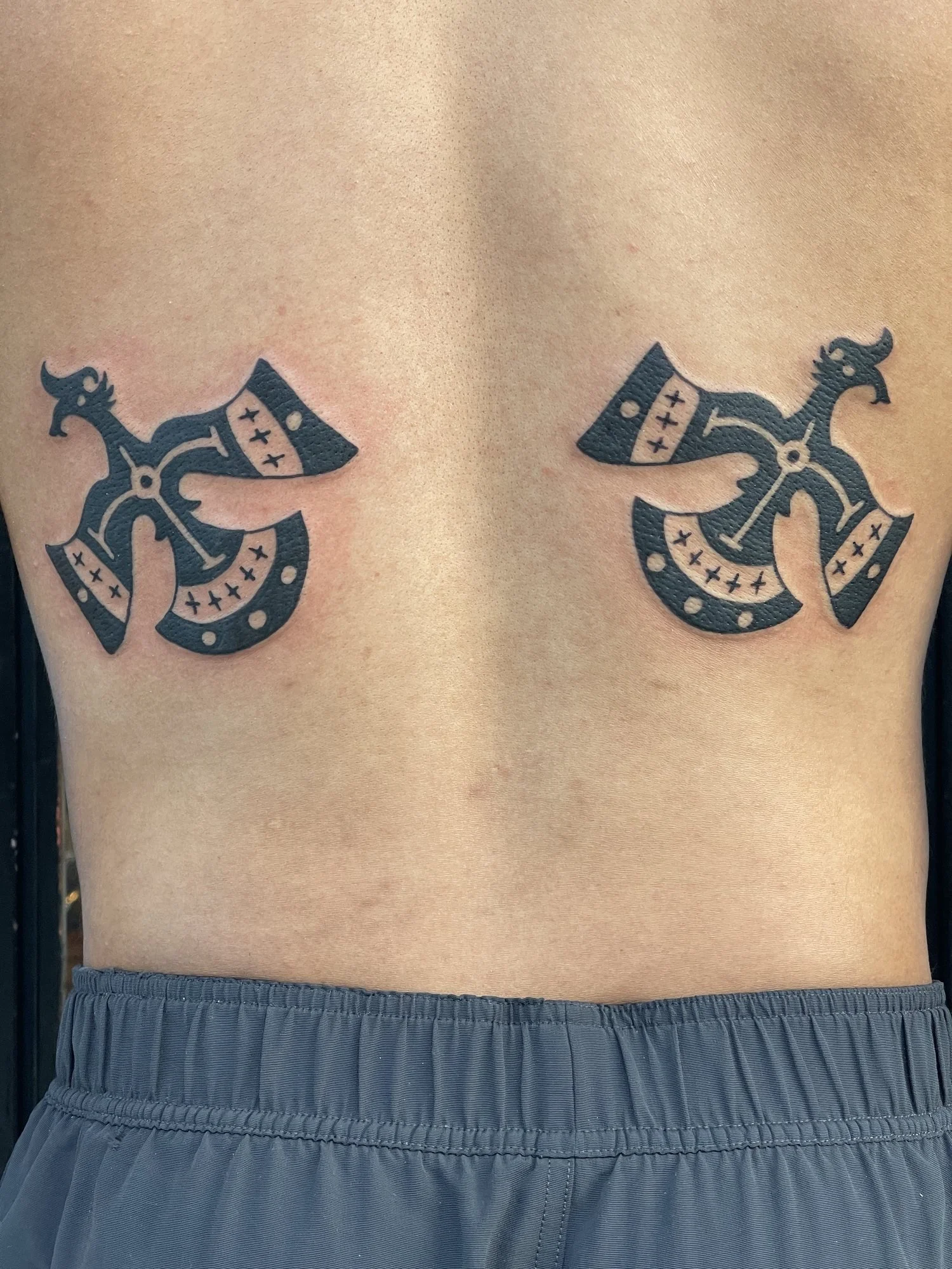Two ornamental blackwork axes tattooed on a back.jpg