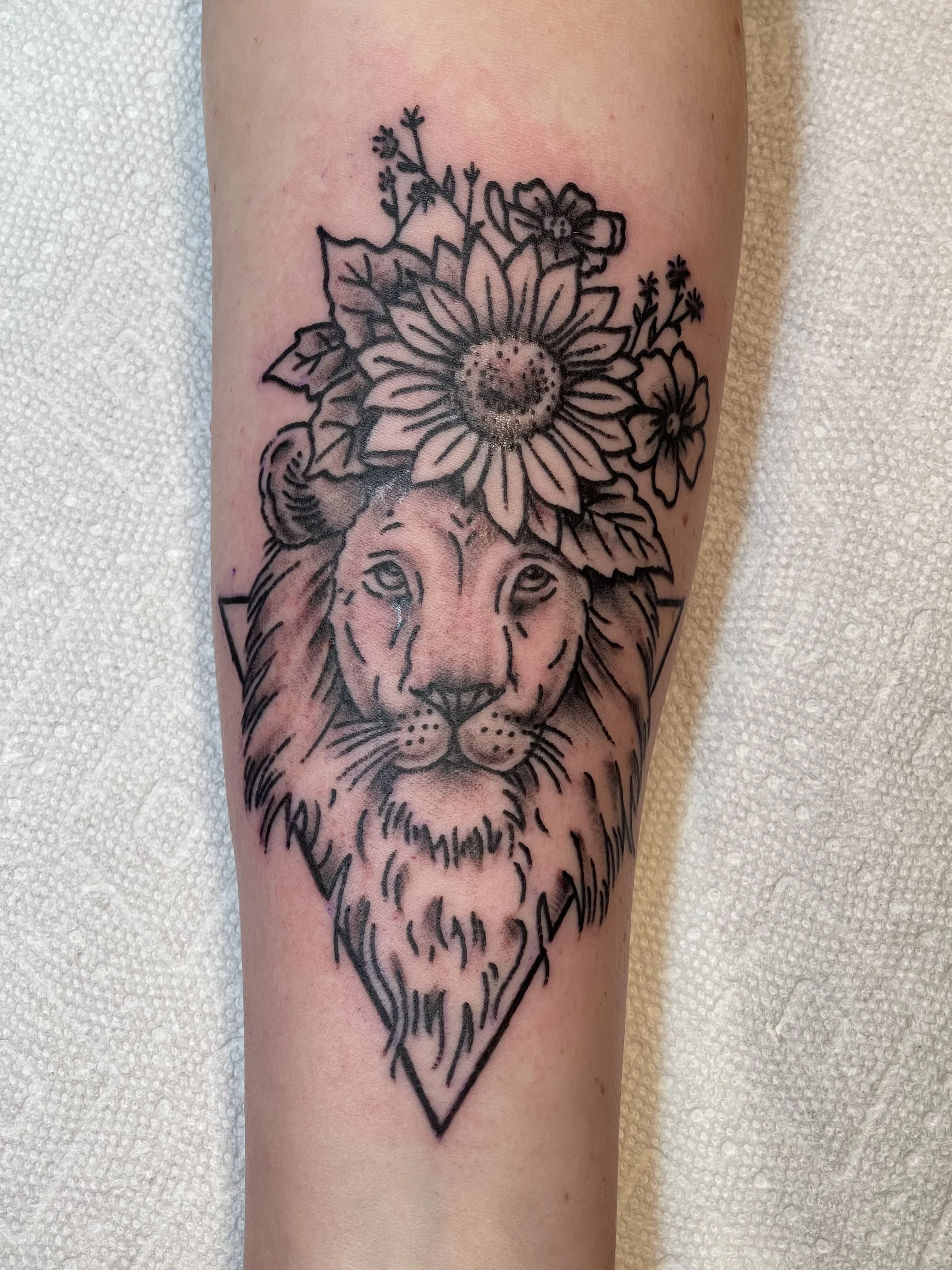 Black and grey lion tattoo with flowers on the forearm by Electric Lotus Tattoo in NYC