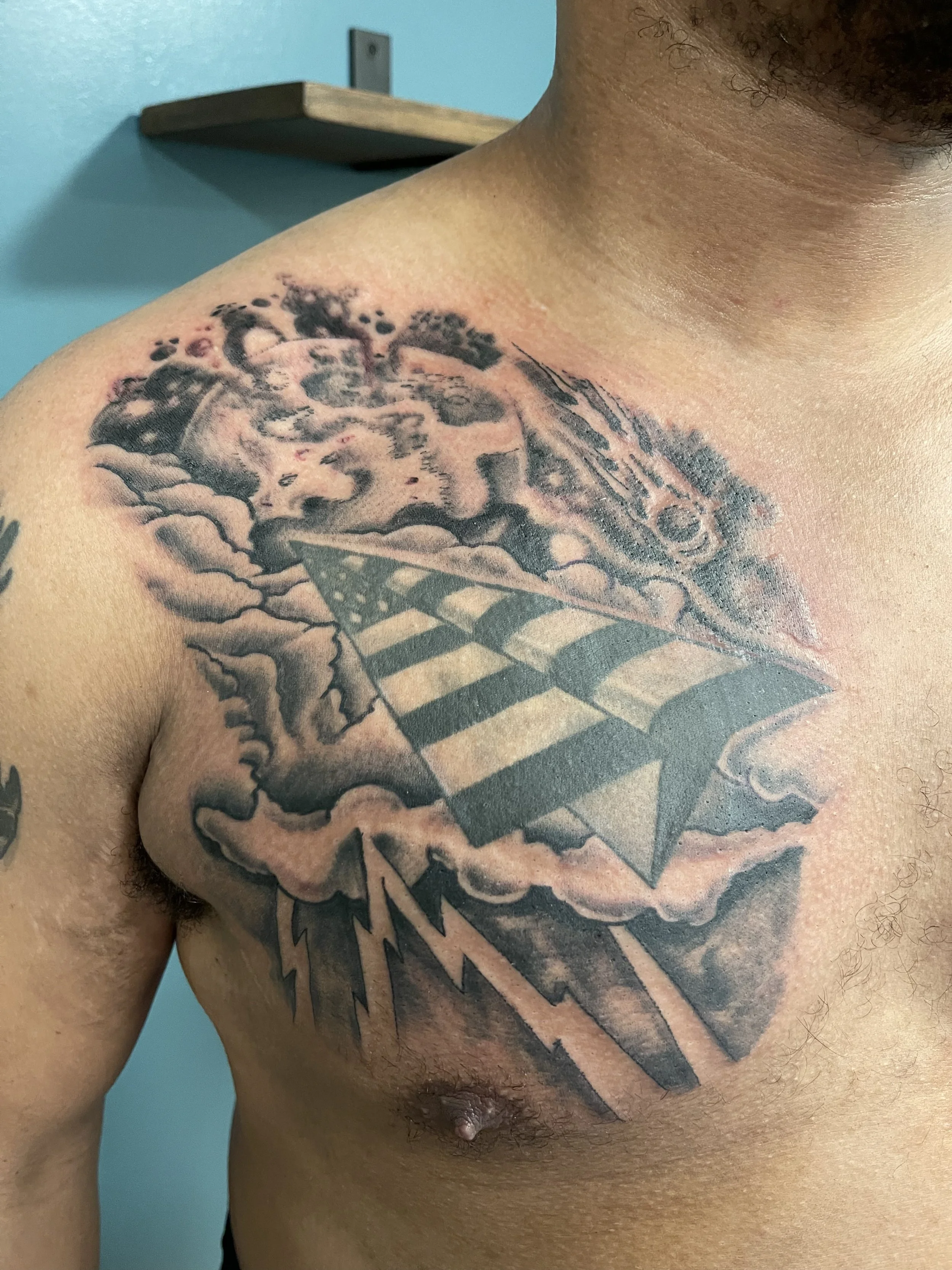 Black and grey peper airplane flag tattoo with clouds on the chest by Electric Lotus Tattoo in NYC