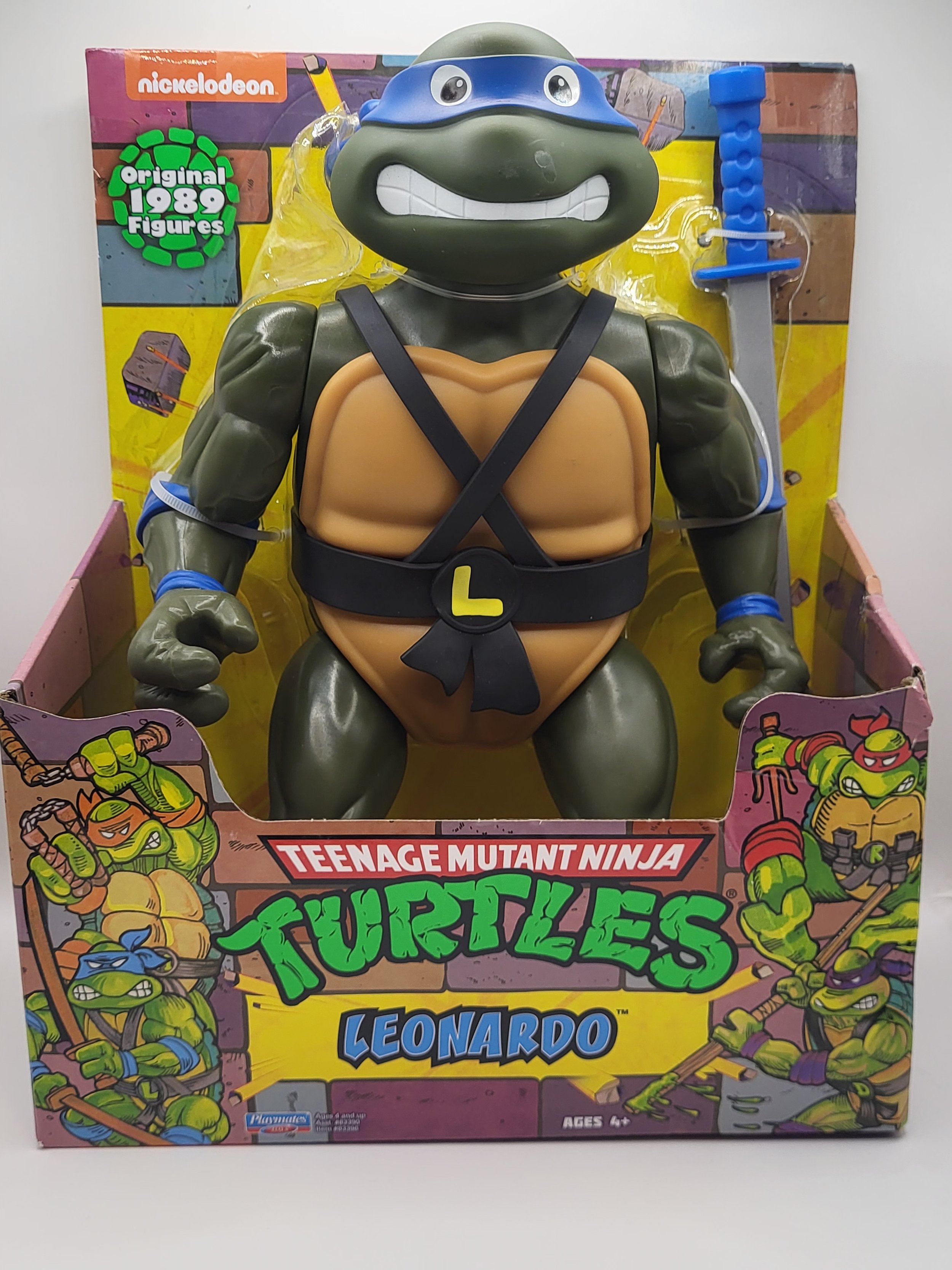 A Teenage Mutant Ninja Turtles Leonardo action figure in its original packaging, featuring Leonardo's head with a blue mask, a green turtle body, and weapons attached, with colorful Turtle artwork on the box.