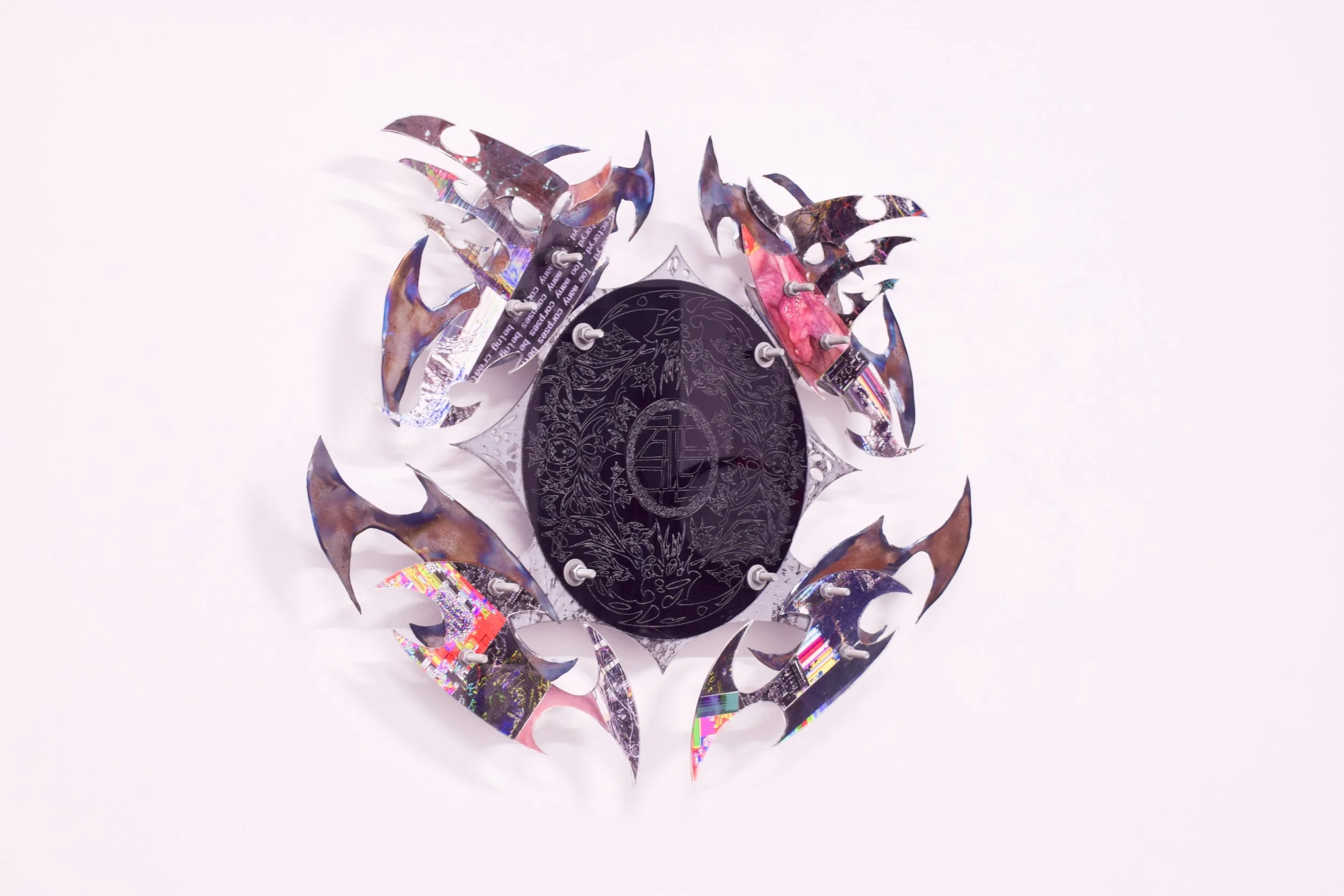 Decorative wall art consisting of a black oval centerpiece with intricate floral patterns, surrounded by metallic, colorful, flame-shaped ornaments arranged in a circular pattern.