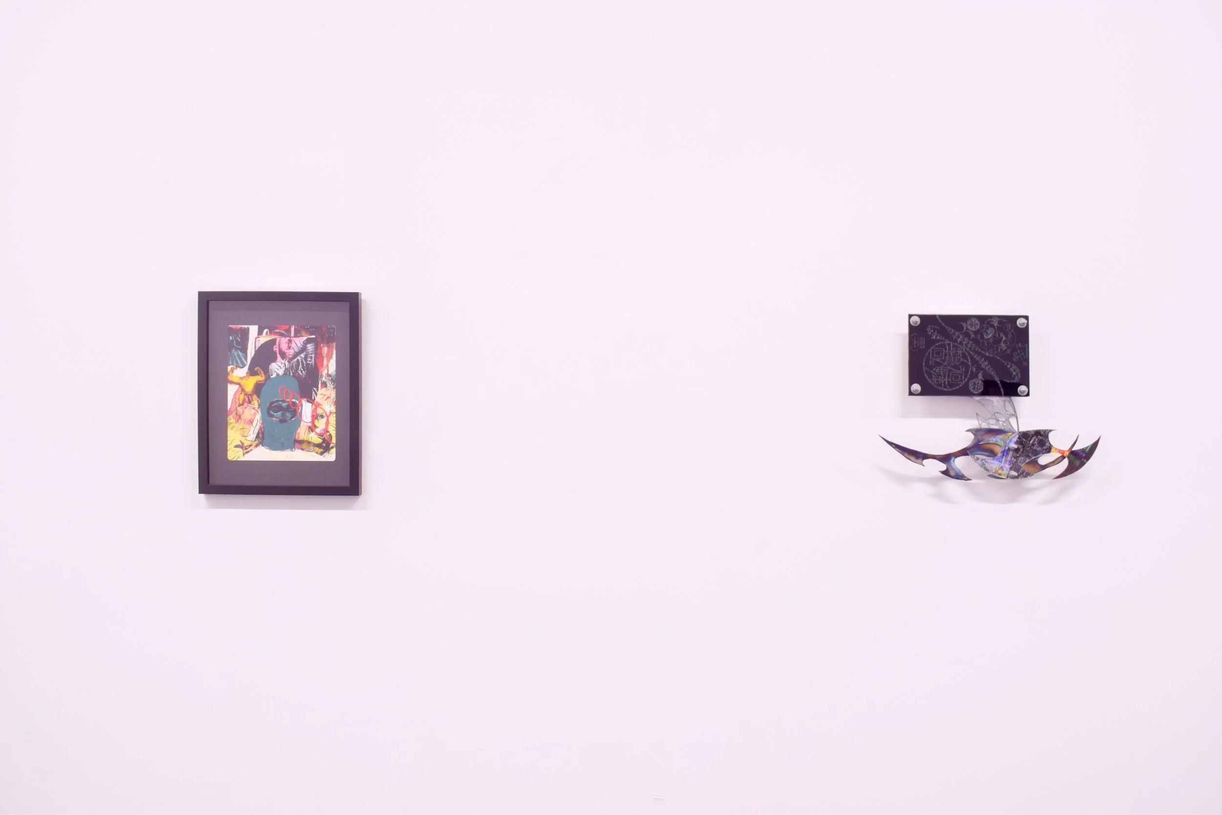Art gallery wall displaying a colorful framed painting on the left and a black plaque with a metal sculpture of a prehistoric fish on the right.