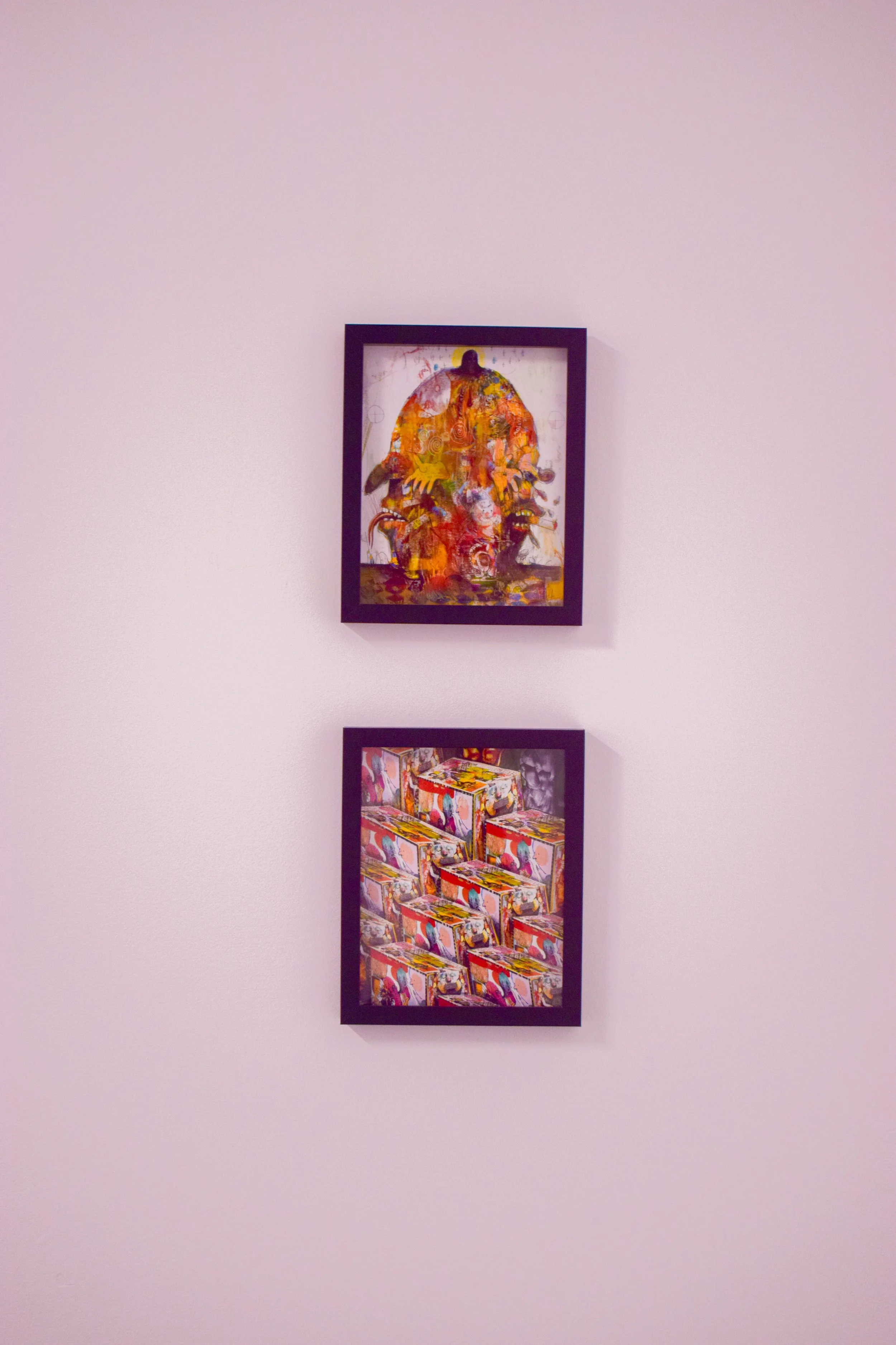 Two framed abstract paintings hung vertically on a pink wall, one above the other.