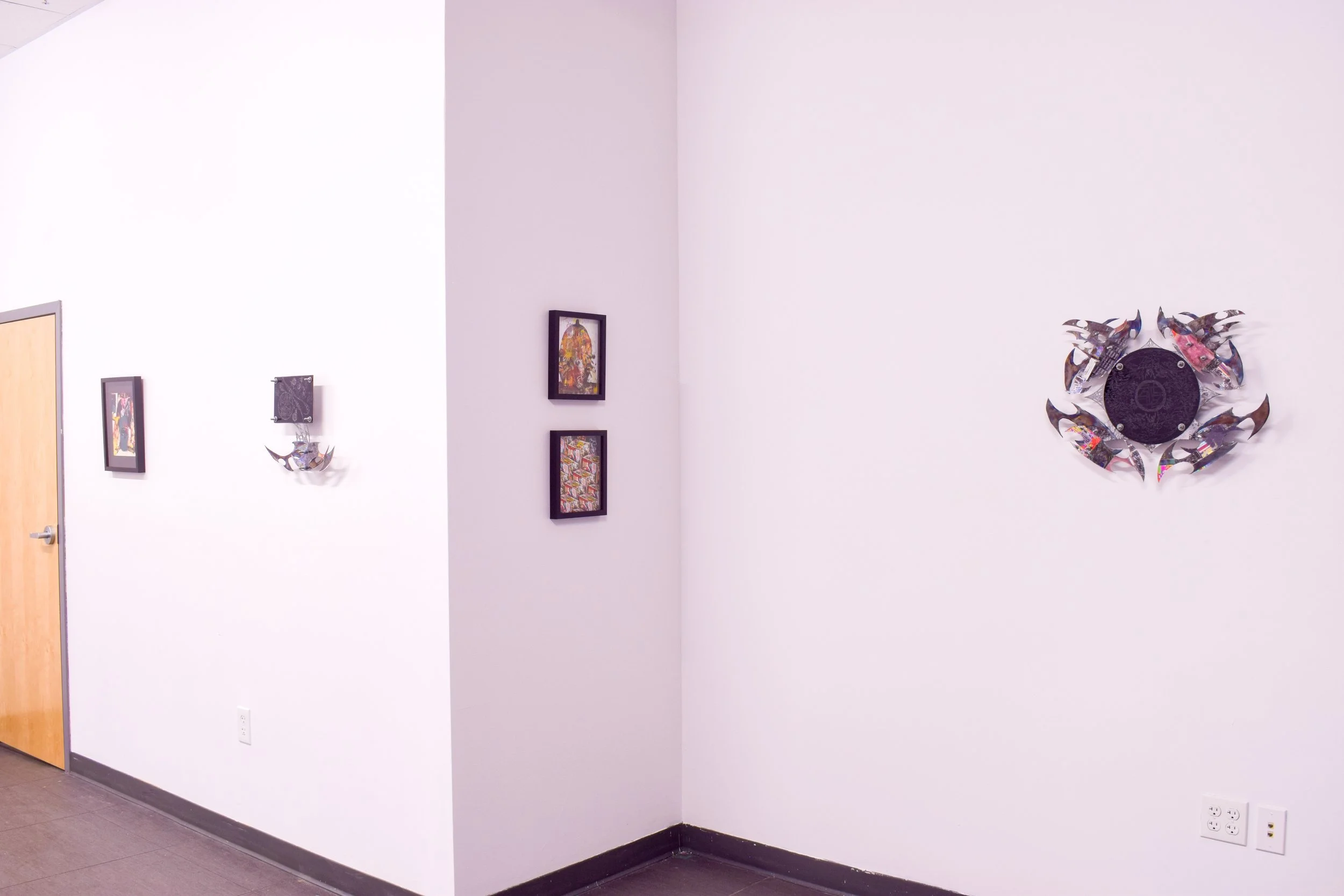 Art gallery wall with framed artwork and a metal sculpture on a white wall.
