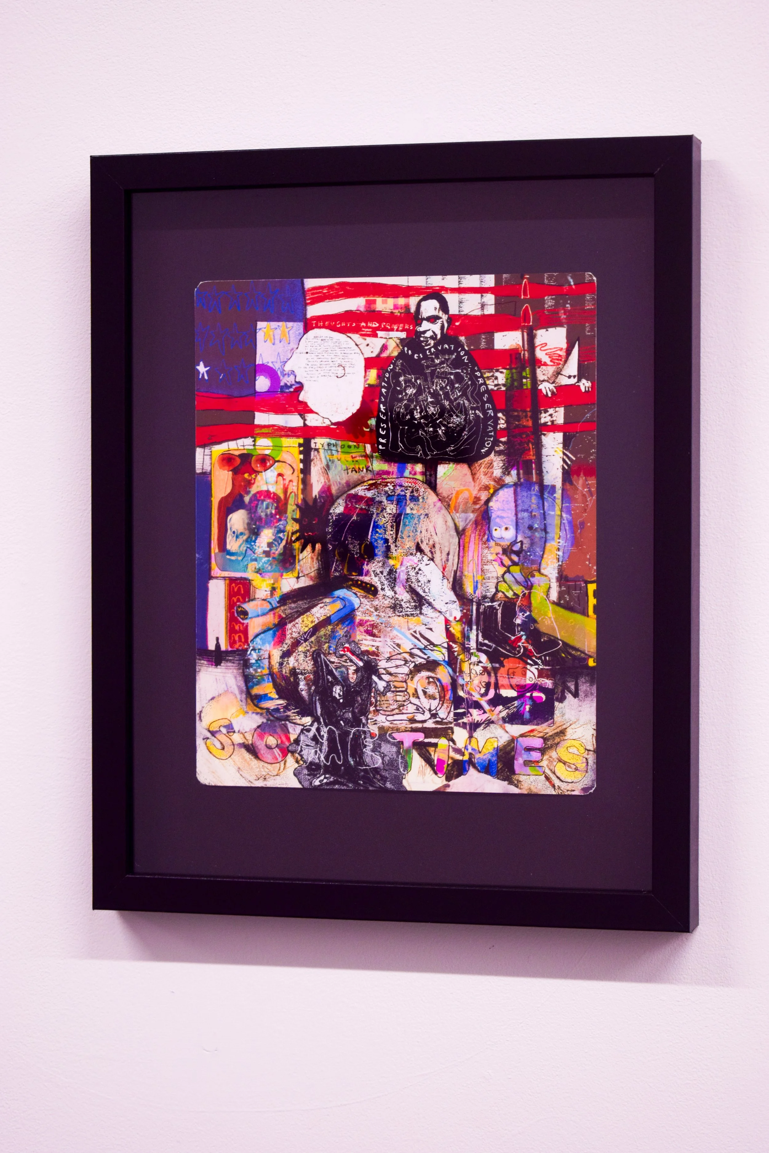 A framed abstract collage artwork featuring various graffiti-style images, text, and characters, including American flag elements and colorful illustrations.