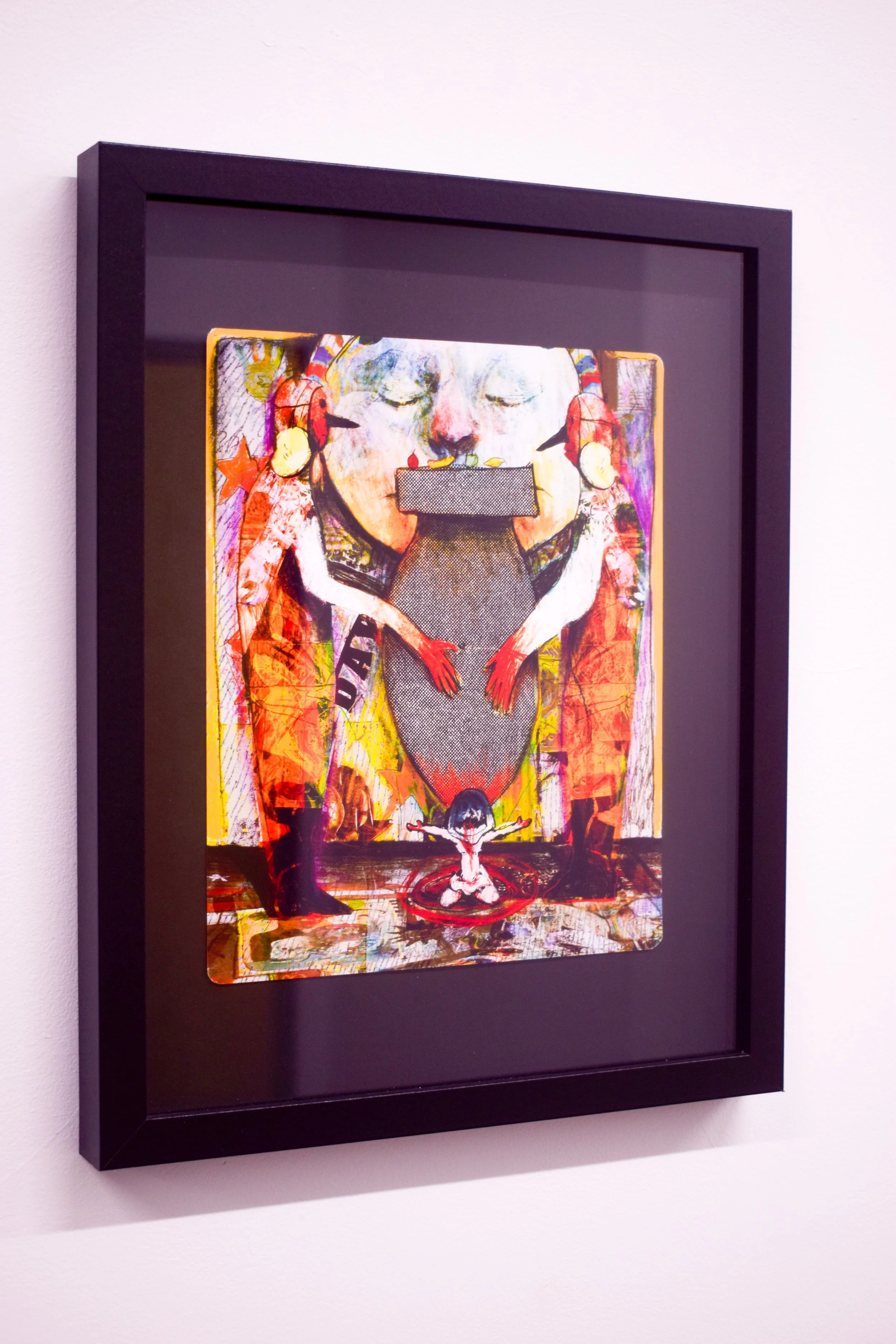 Colorful artwork depicting abstract figures, including a large face with closed eyes and a small figure with arms outstretched, framed in black and mounted on a white wall.