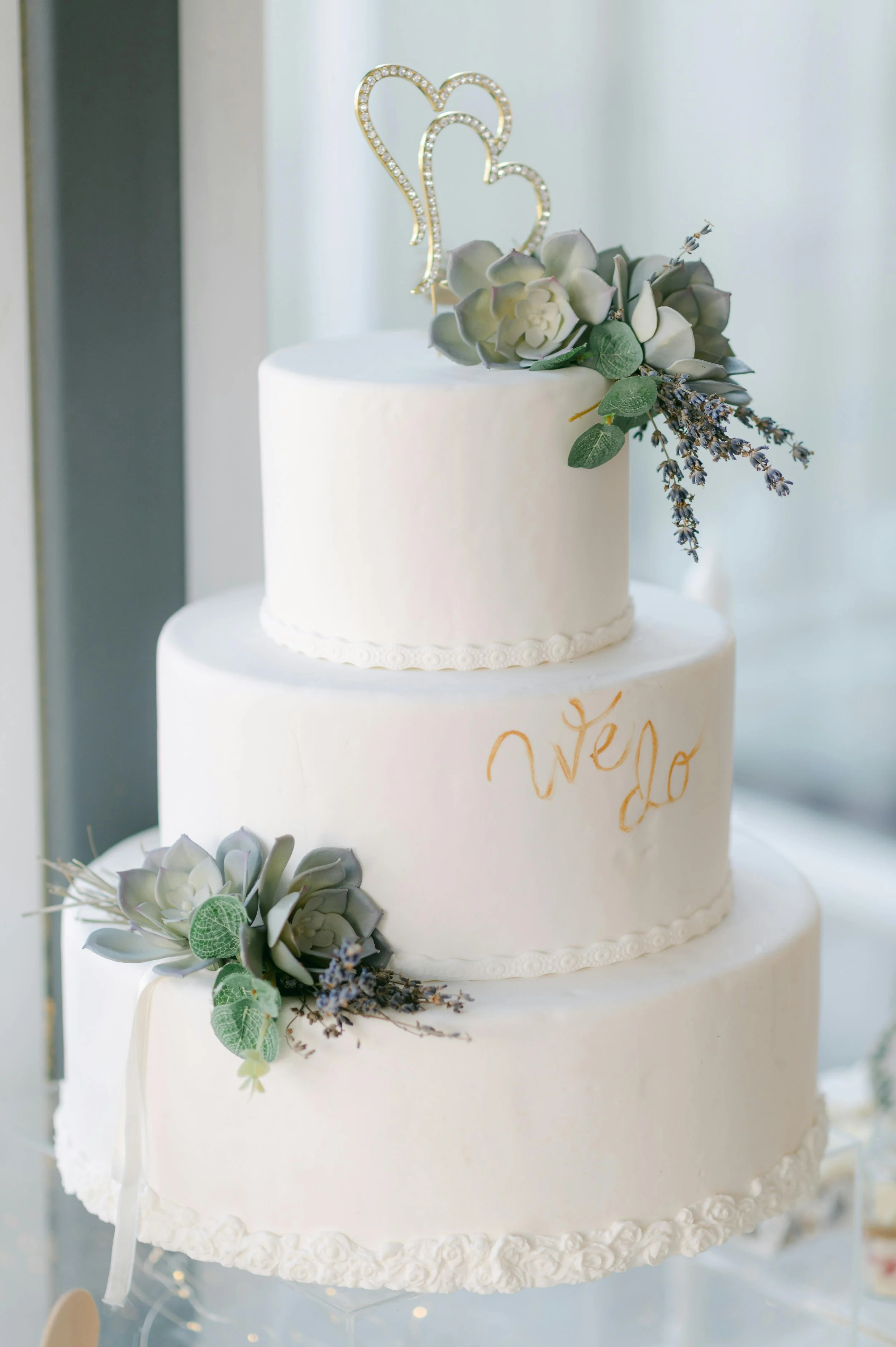 Four-tier white wedding cake adorned with pink and white roses on a decorative stand.