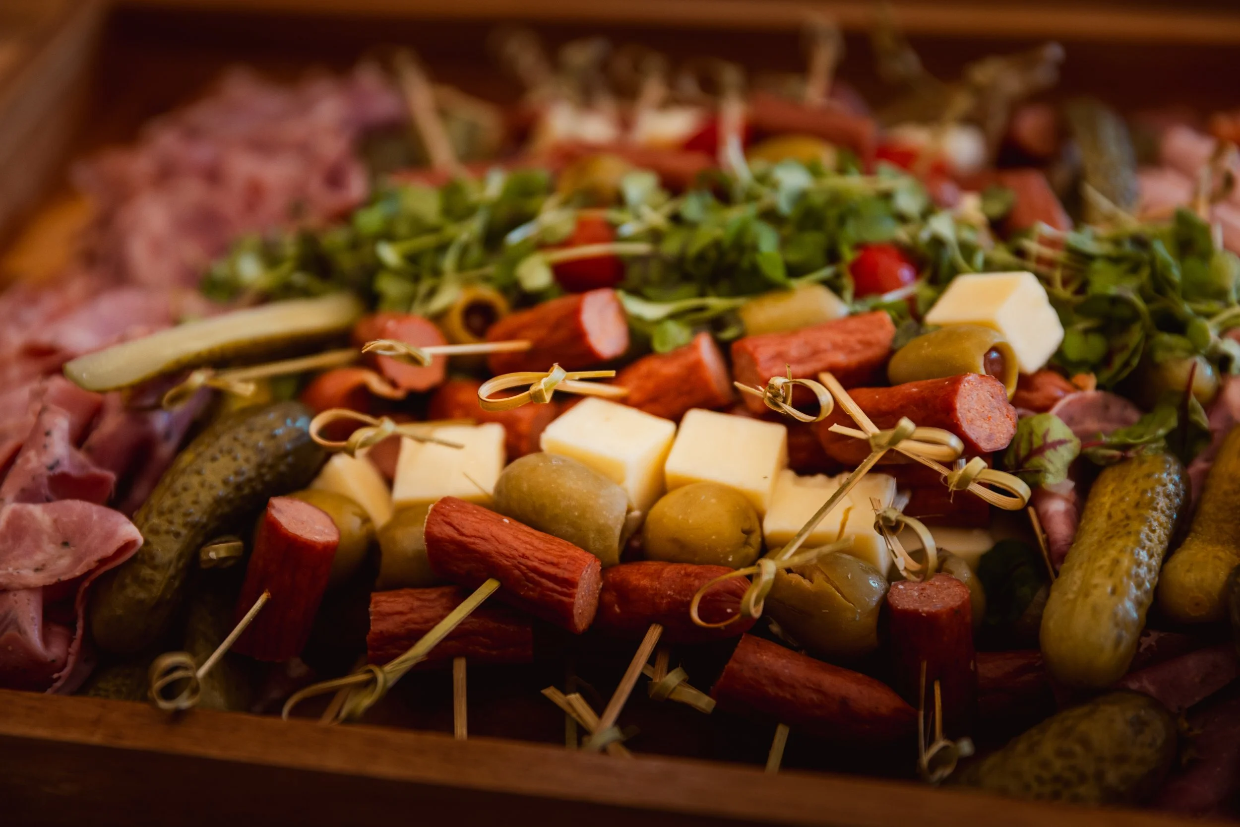 Cheese and charcuterie board with assorted cheeses, cured meats, crackers, macarons, fruits, and nuts, accompanied by a bowl of olives.