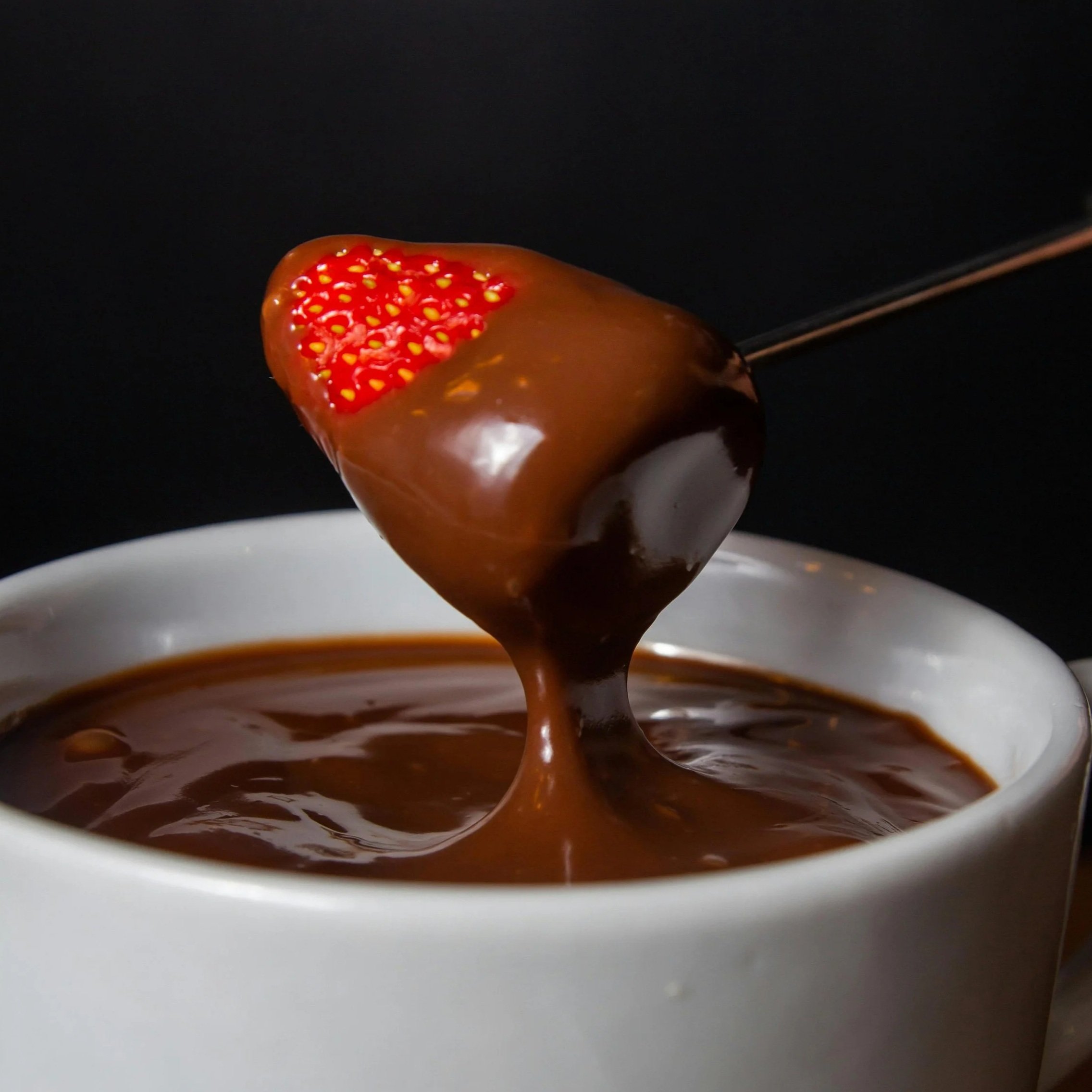 Strawberry being dipped in melted chocolate with other strawberries nearby.
