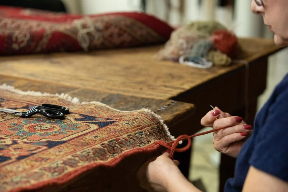 Specialist repairing the edge of an oriental rug by hand with a needle and thread