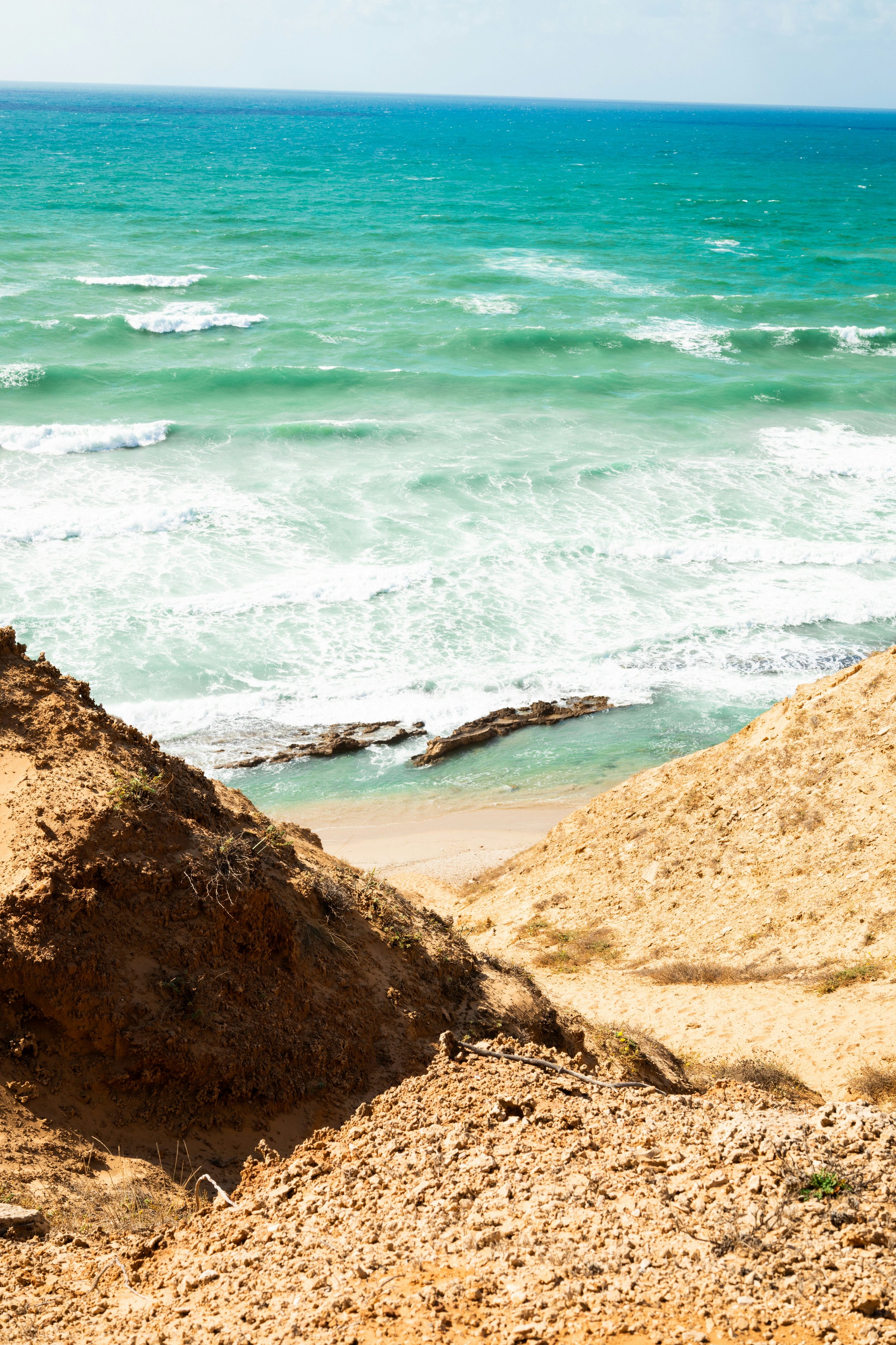 Aerial view of a coastal scene with sandy dunes in the foreground and turquoise ocean waves in the background.