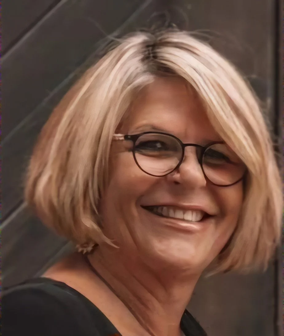 A smiling woman with blonde, shoulder-length hair wearing glasses.