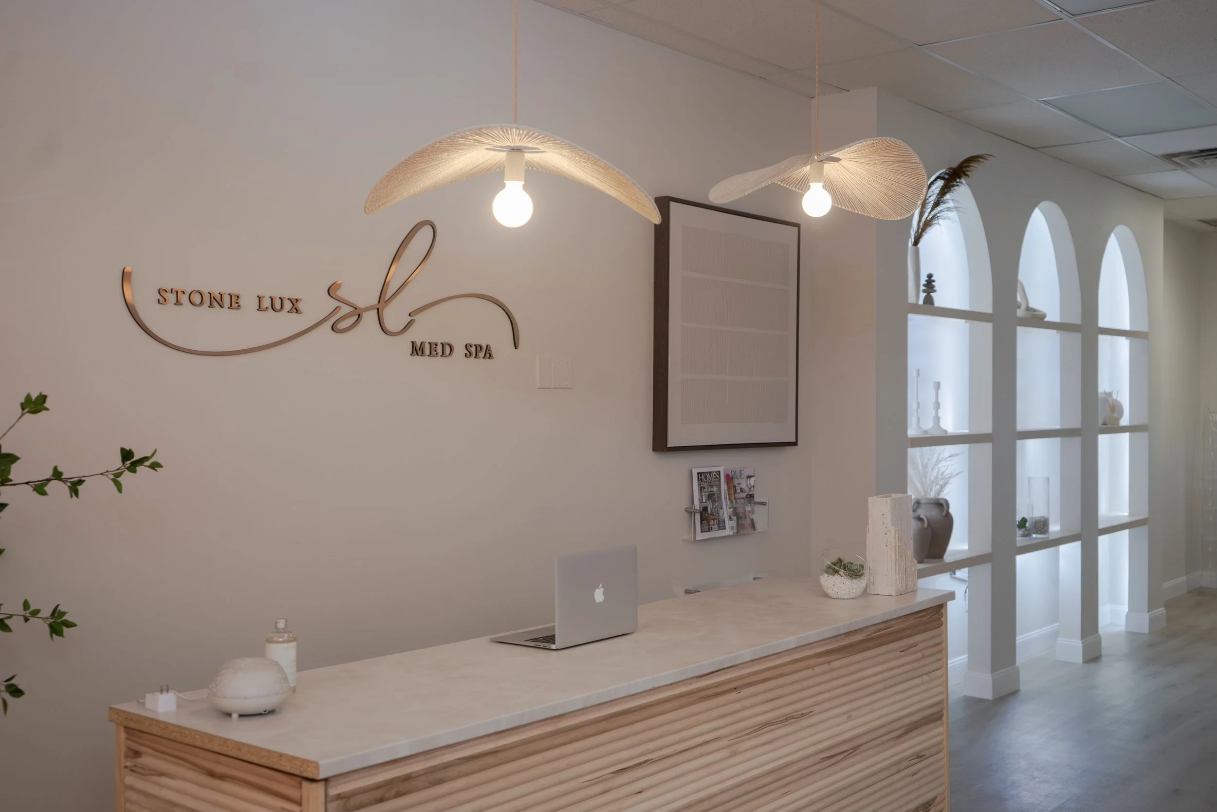 Reception desk at Stone Lux Med Spa with wooden accents, decorative lighting, and magazine rack.