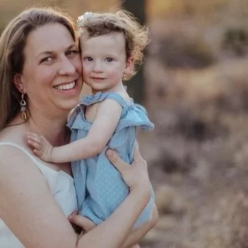 Woman holding a young girl outdoors, both smiling