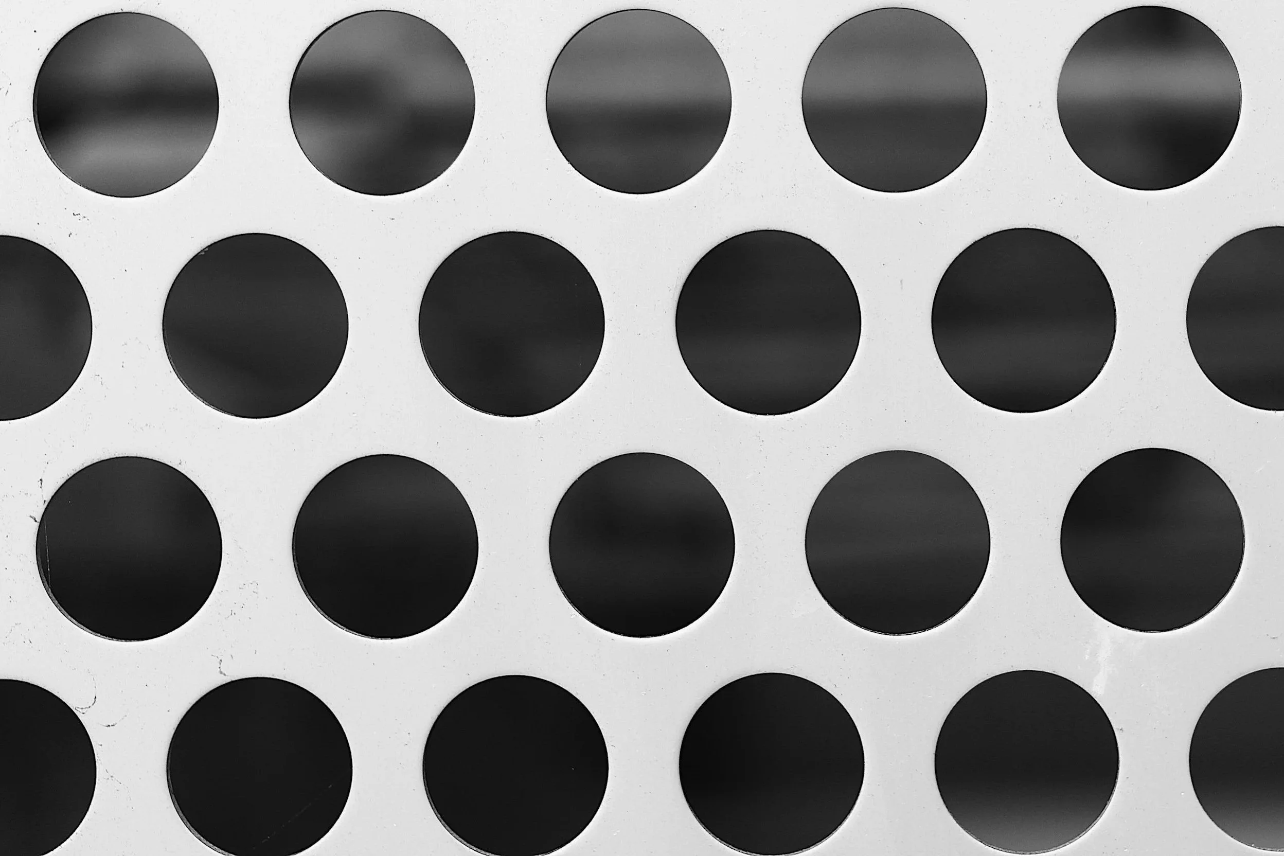 Close-up of a sheet with multiple round black stickers arranged in rows on a white background.