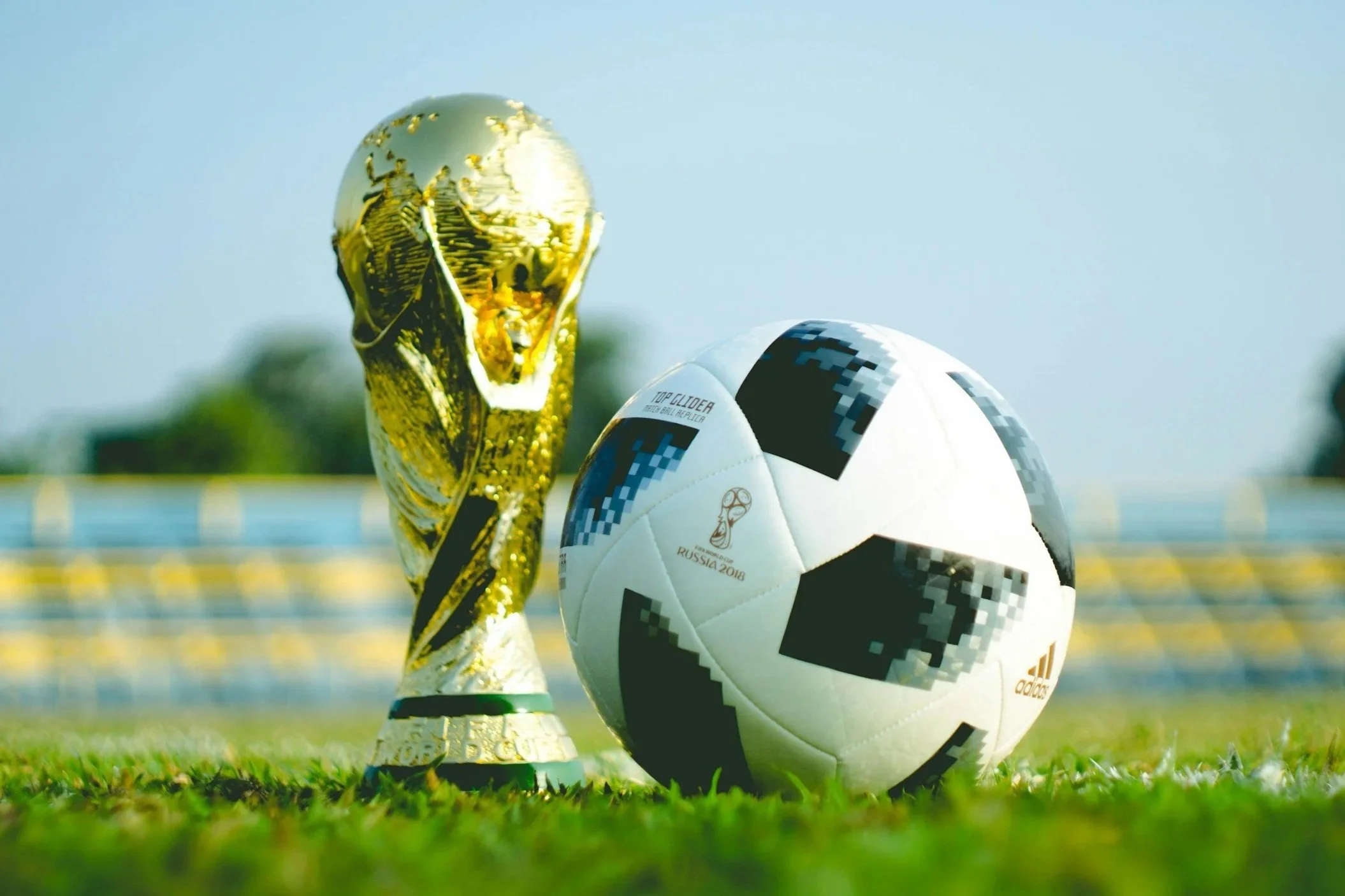 A gold trophy, a FIFA World Cup Russia 2018 soccer ball, and a FIFA World Cup Russia 2018 official match ball on a grassy field.