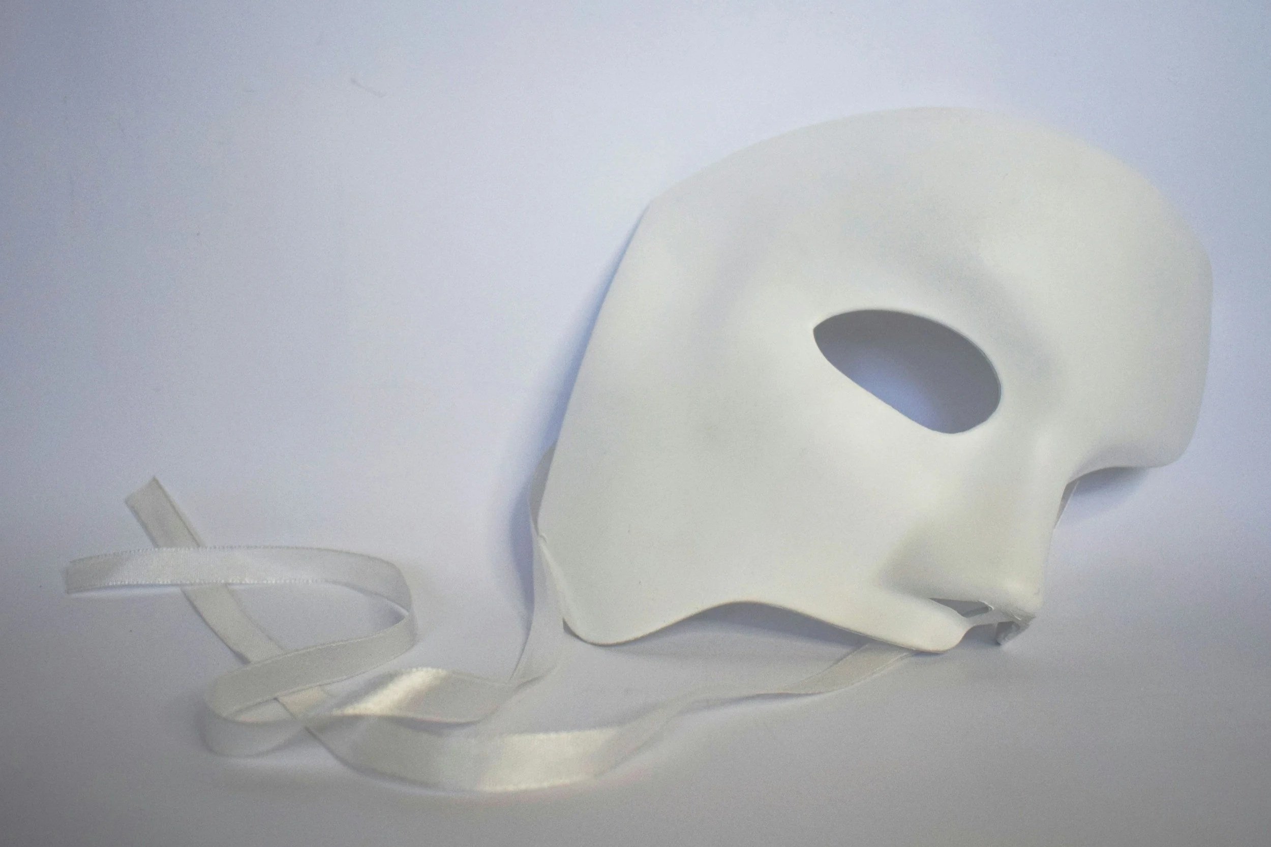 White theater mask with satin ribbons on a plain white background.