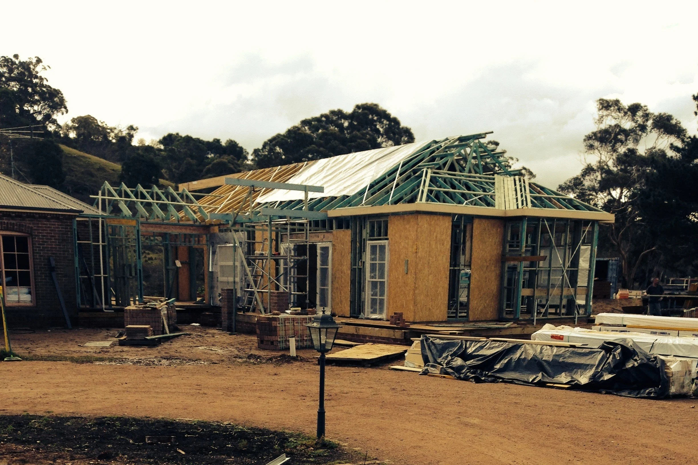 House under construction with exposed framework and partially installed roof, construction materials and scaffolding around the site.