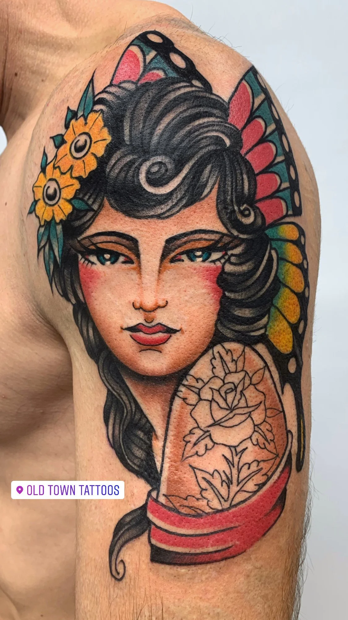 Tattoo of a woman with dark hair, flowers, a butterfly wing headdress, and a floral tattoo on her shoulder, located at Old Town Tattoos.