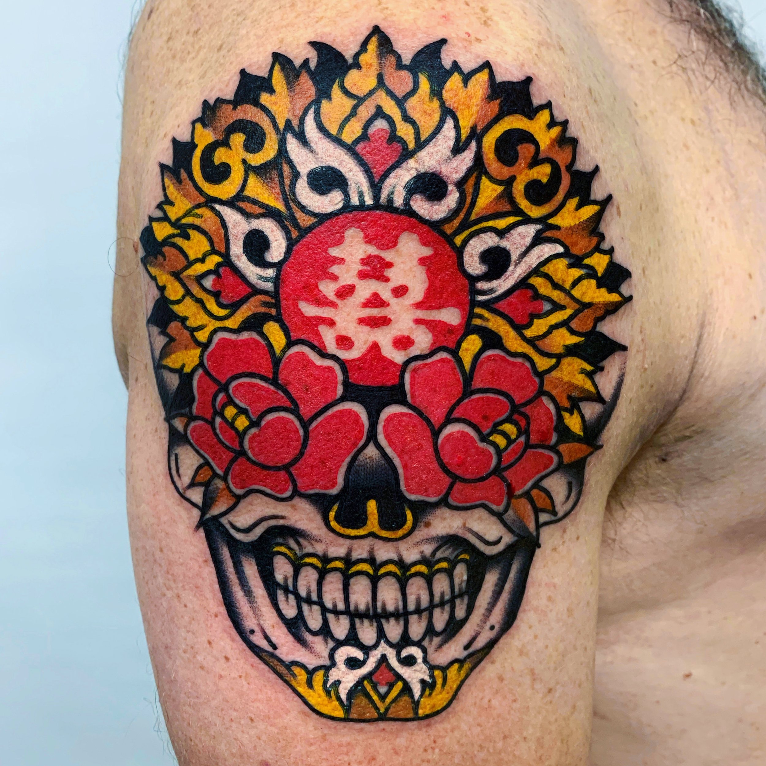 Colorful tattoo of a skull with floral and decorative elements on a person's shoulder.