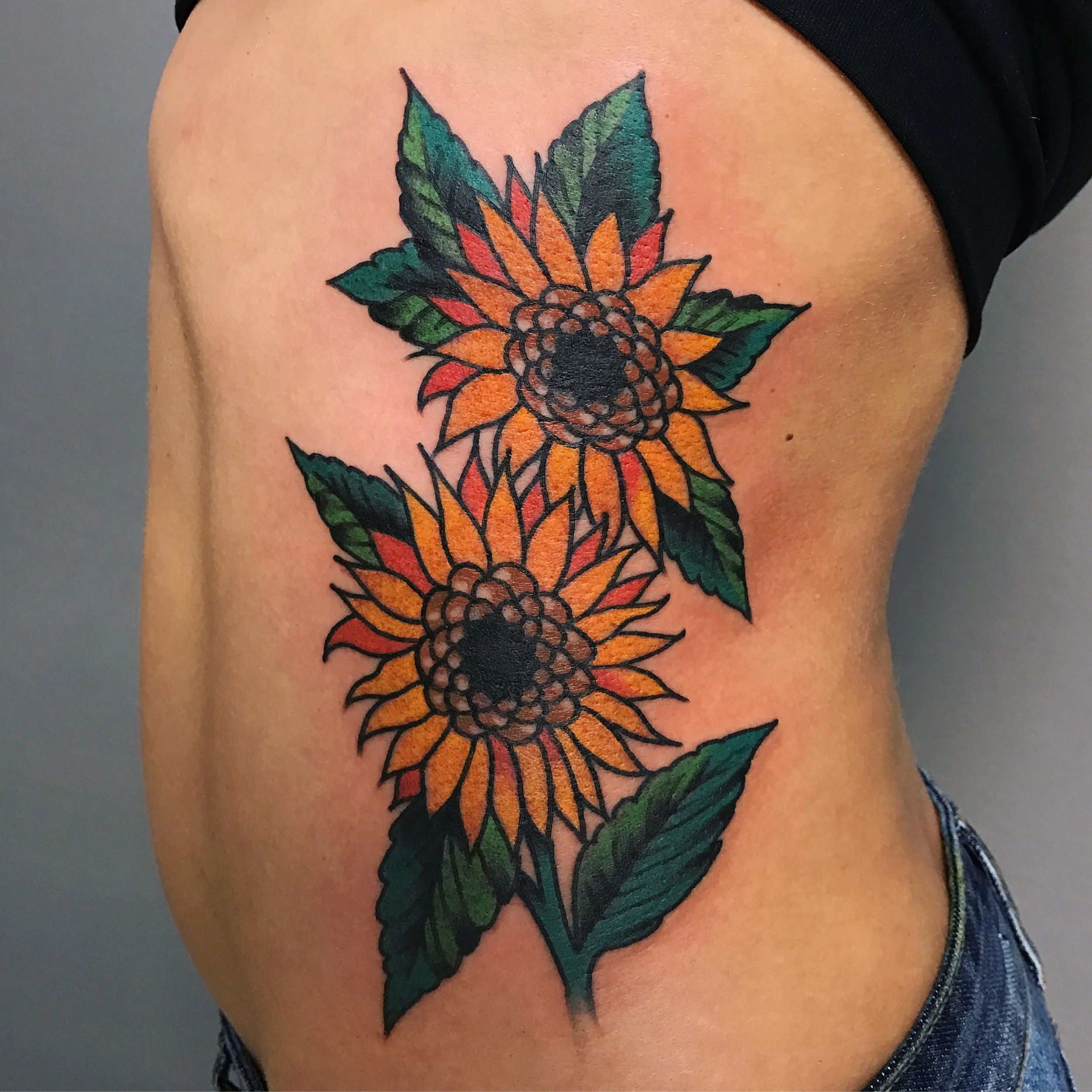 Tattoo of two sunflowers with green leaves on a person's side torso.