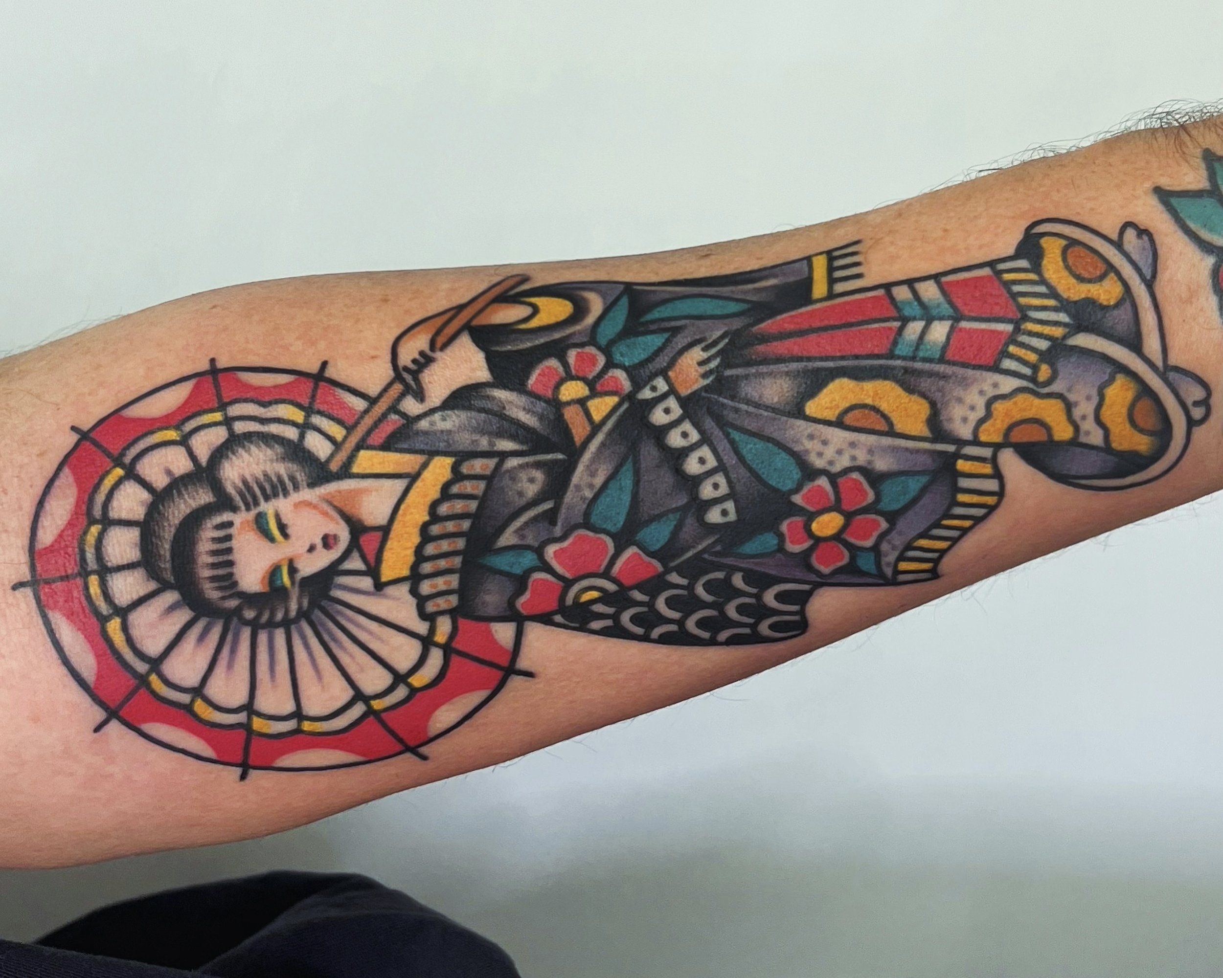 Tattoo of a geisha holding a parasol with colorful floral designs and traditional Japanese patterns on arm.
