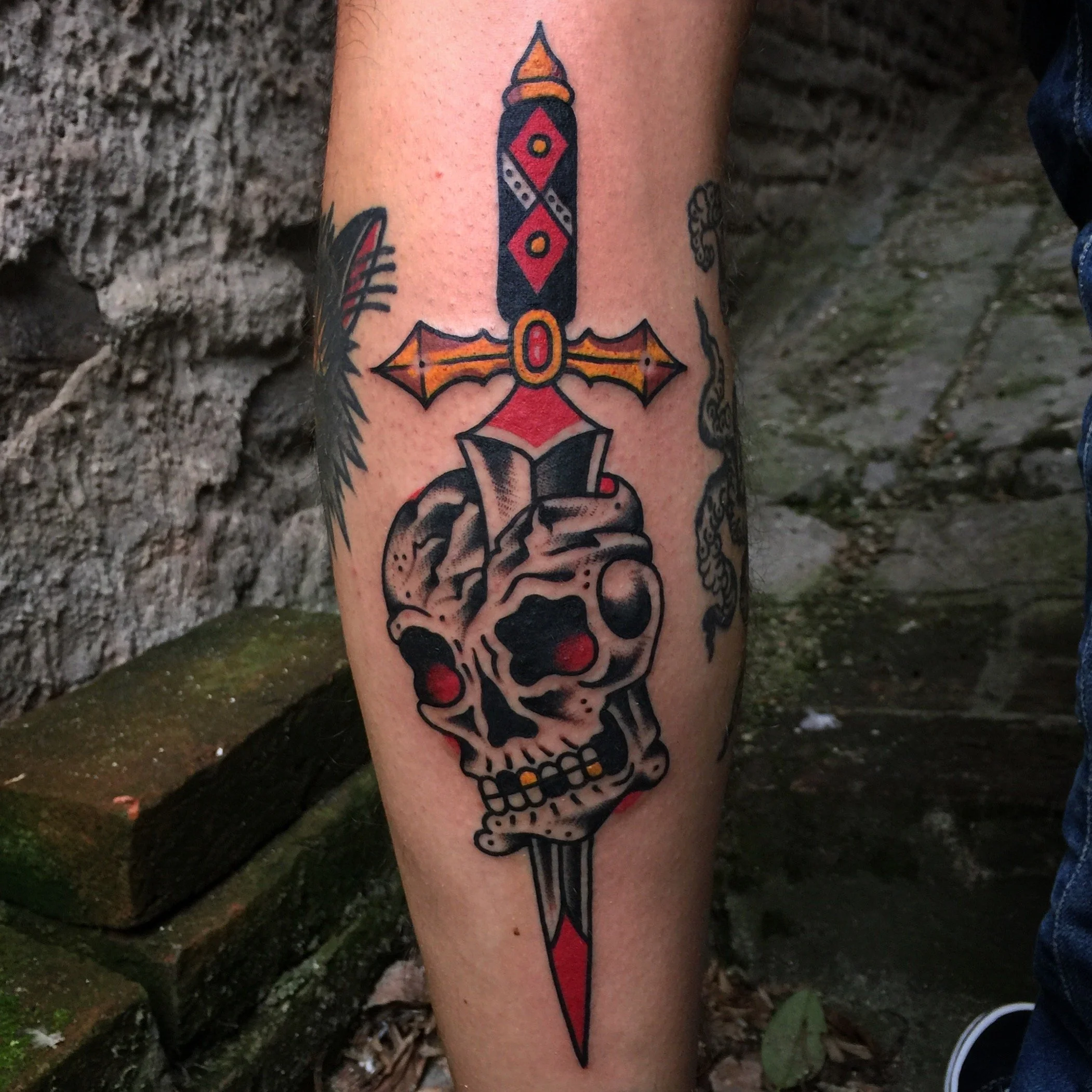 Tattoo of a skull with a sword through it, and a hand holding the sword, on a person's leg.