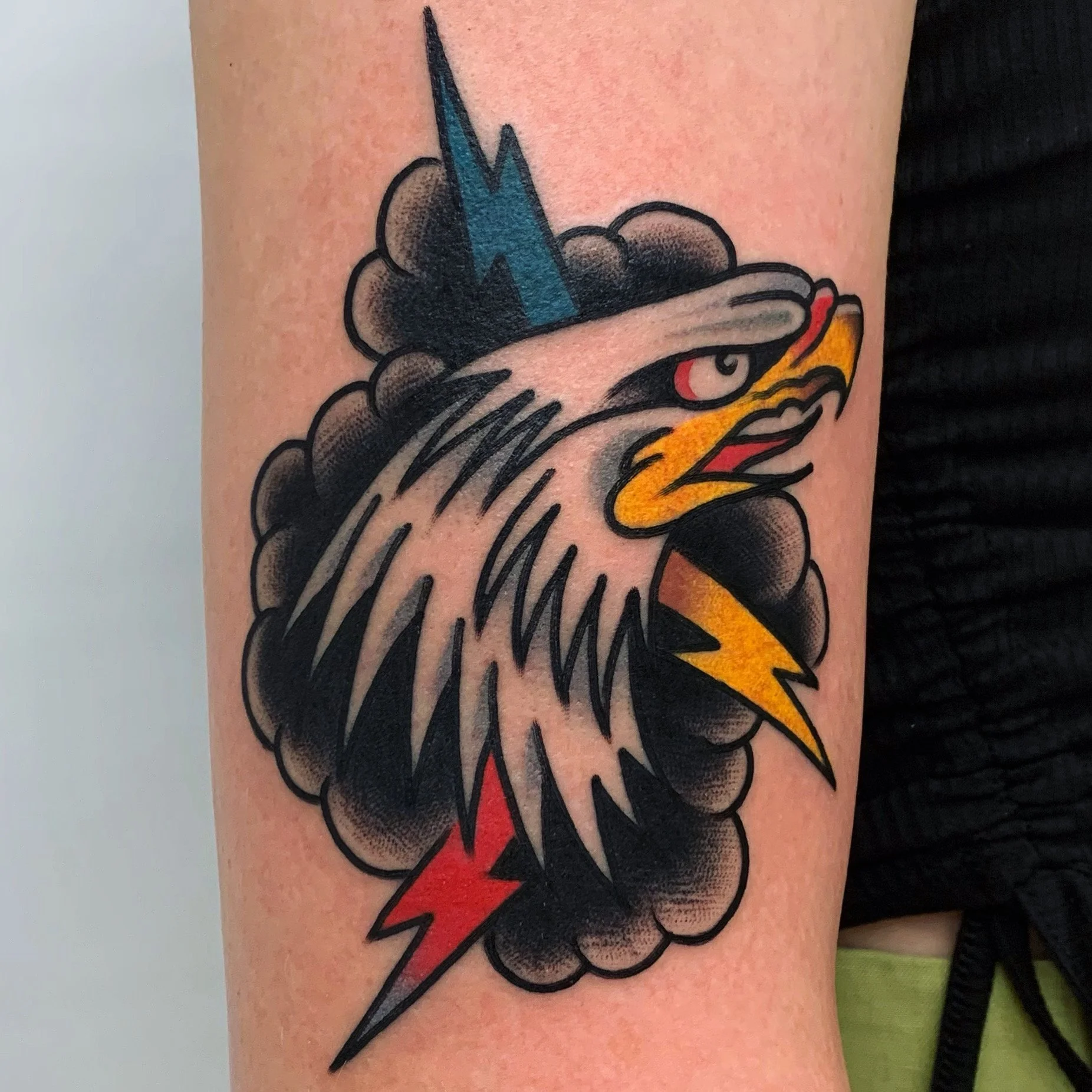 Tattoo of an eagle's head with a blue lightning bolt on its forehead, inside a black cloud with red and yellow lightning bolts.