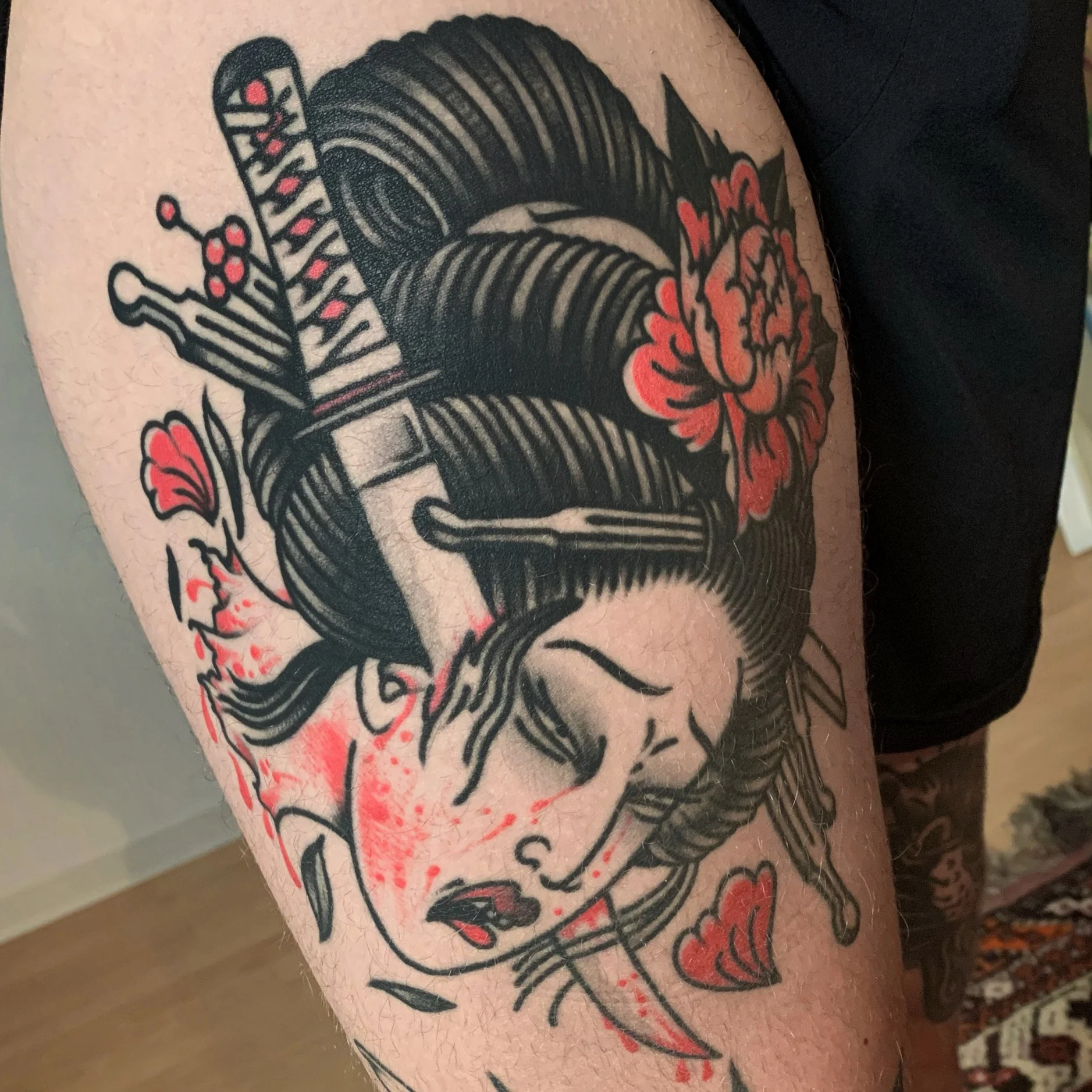 Tattoo of a woman's face with dark, flowing hair, closed eyes, parted lips, surrounded by red flowers, hearts, a dagger, and red splashes.
