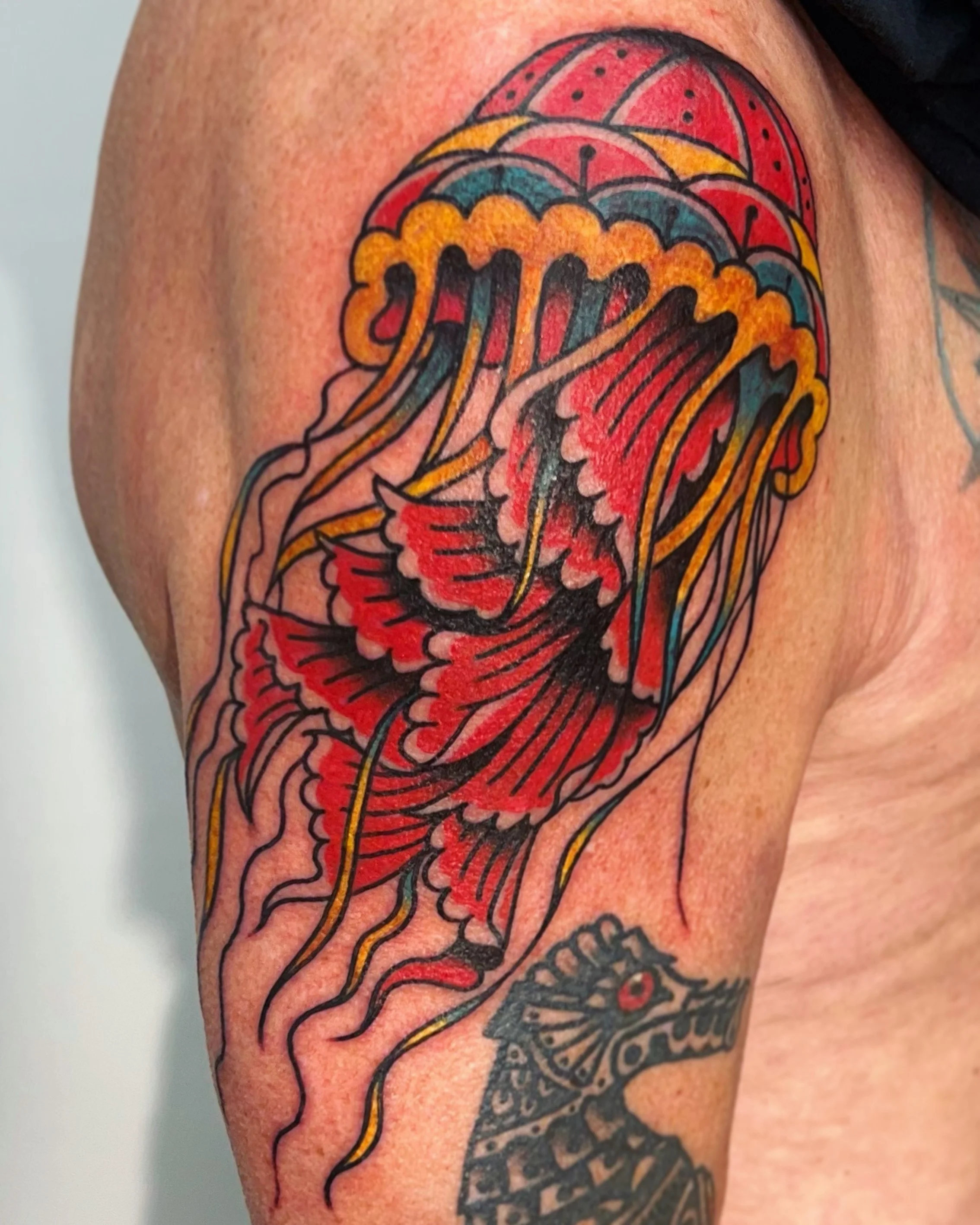 Tattoo of a colorful jellyfish on a person's upper arm.