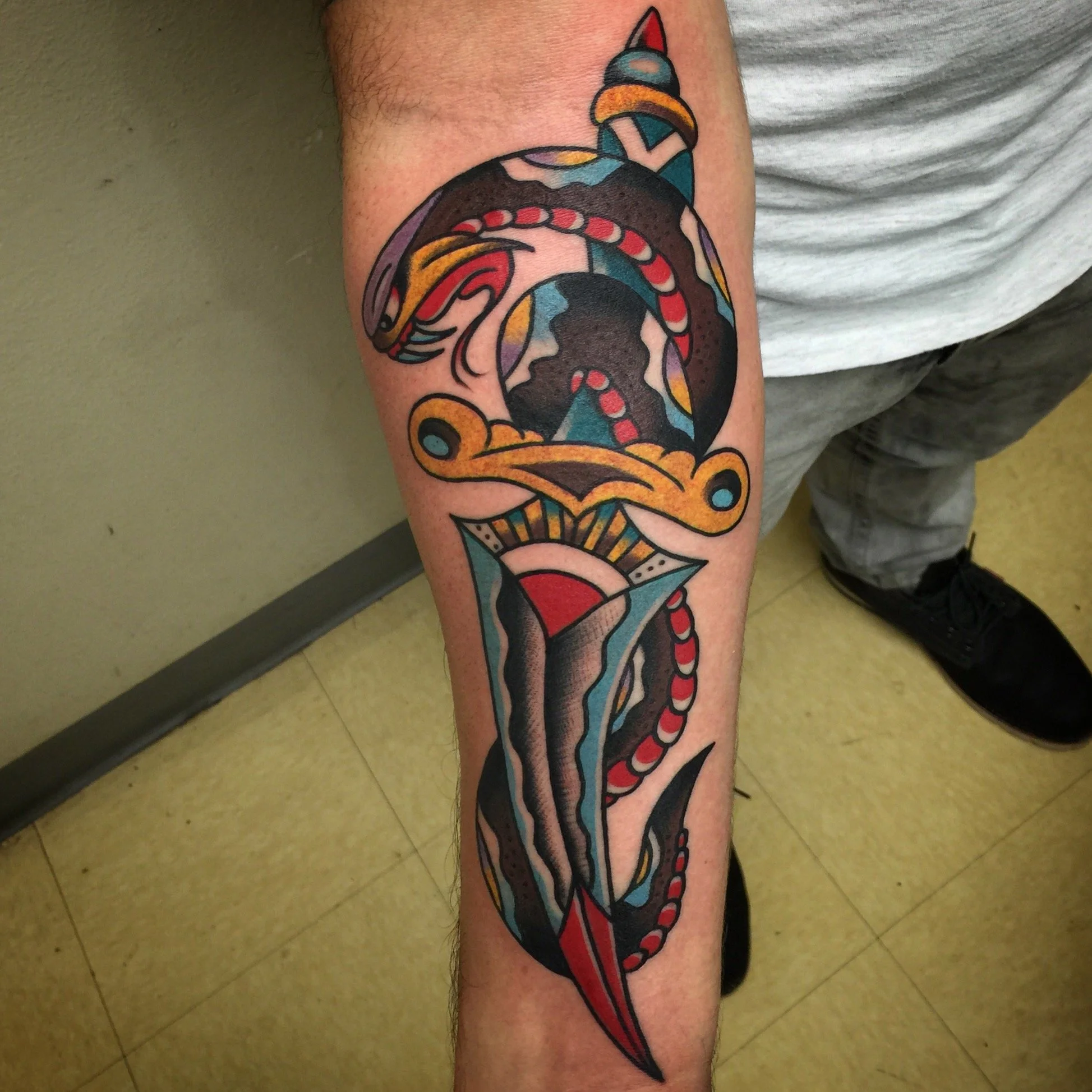 A colorful tattoo of a snake wrapped around a sword on a person's lower leg.