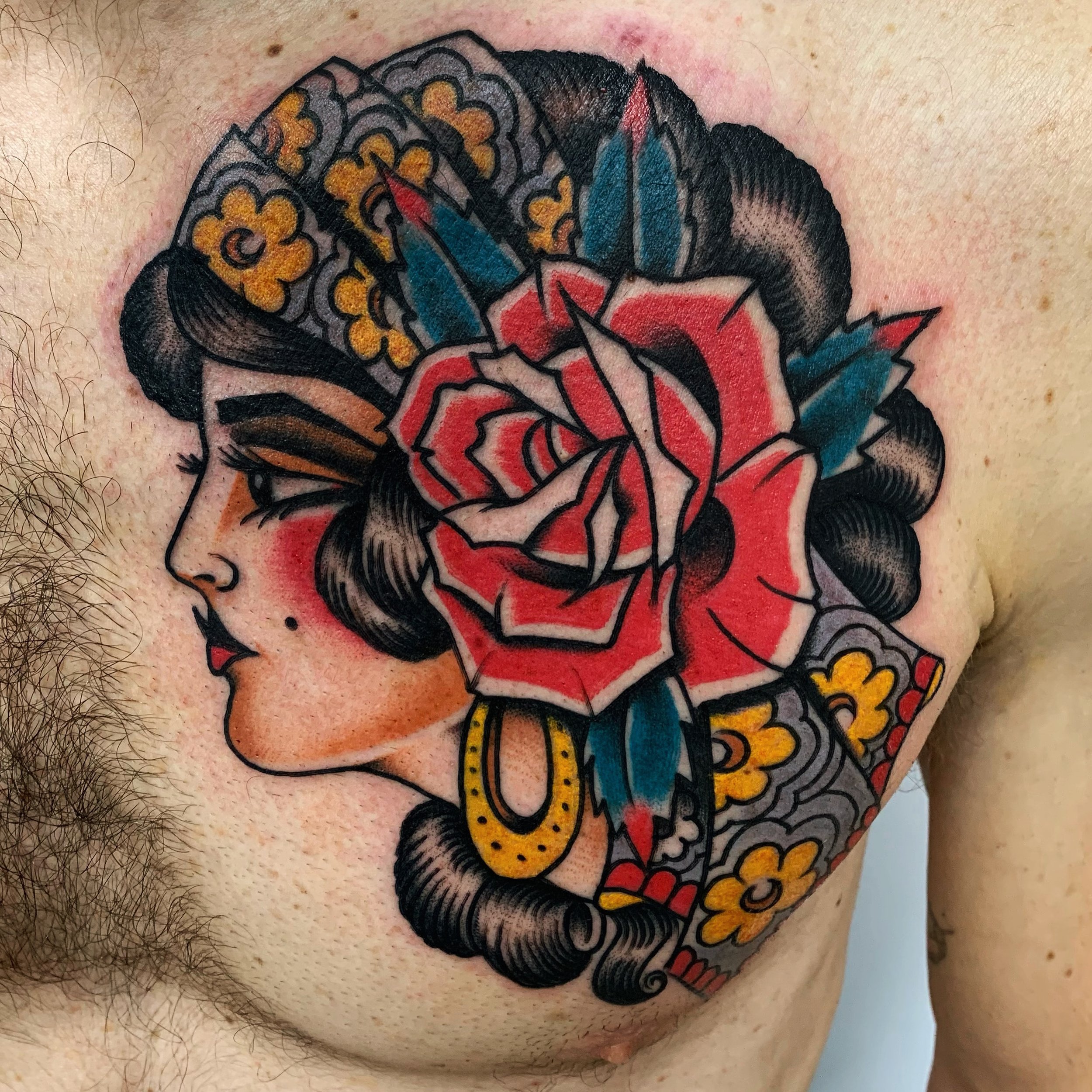 Tattoo of a woman in profile with a large red rose and blue flowers in her hair on a person's chest.
