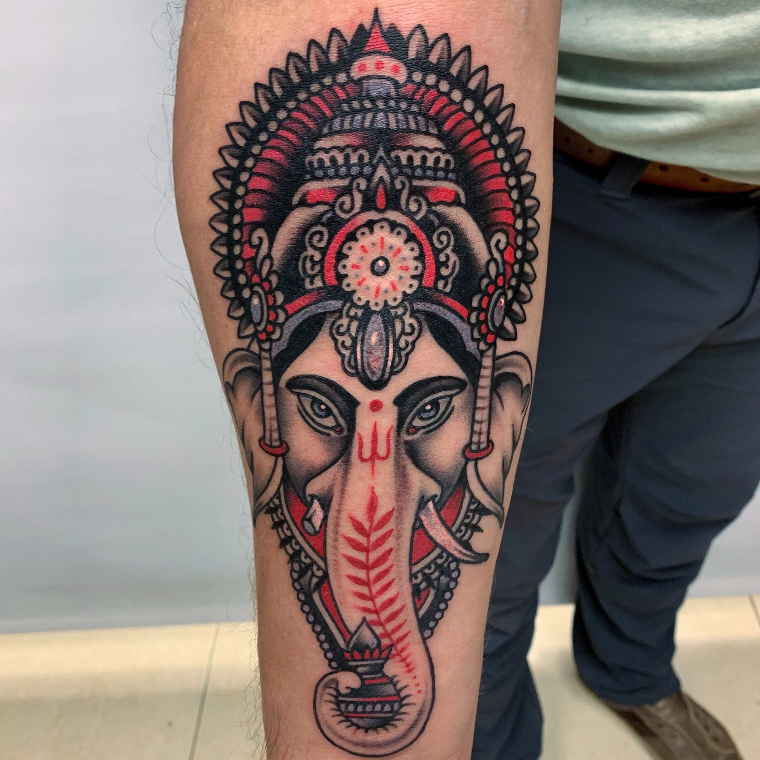 Tattoo of an elephant-headed deity with ornate headdress and jewelry on a person's arm.