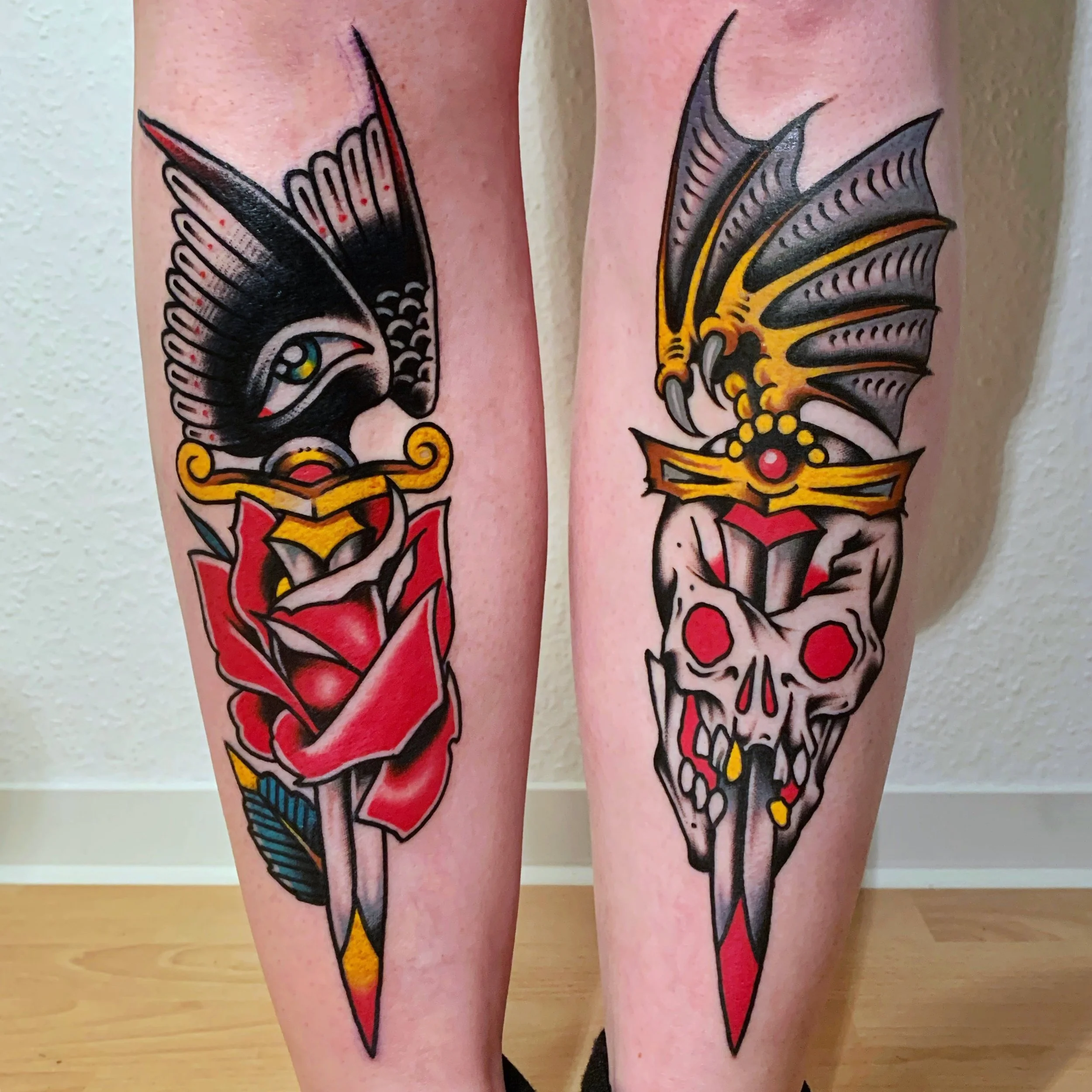 Tattoo of a dagger piercing a skull on one leg and a dagger piercing an eagle on the other leg, done in traditional tattoo style with bold black outlines and vibrant colors.