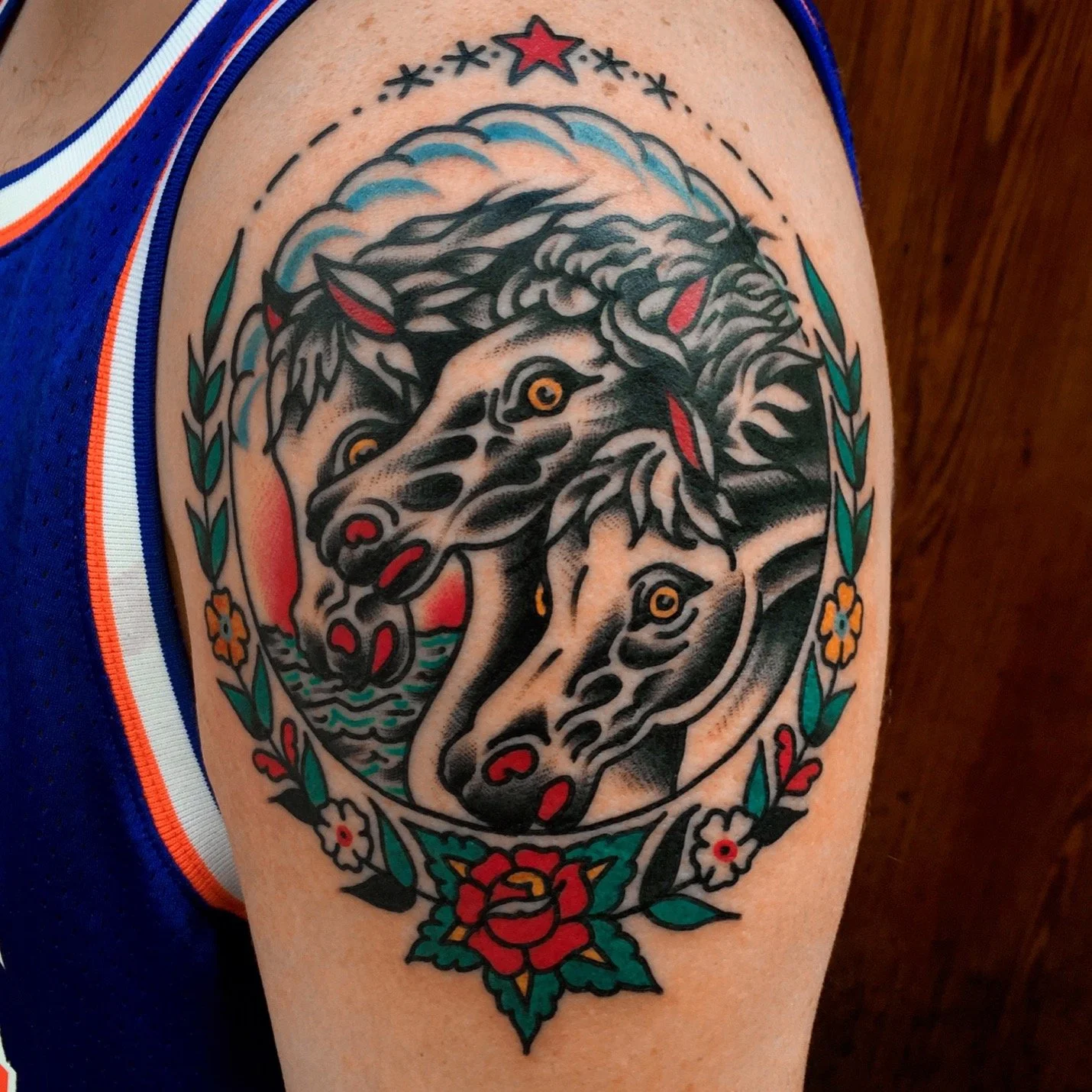 Tattoo of two stylized wolf heads with piercing eyes, surrounded by a floral and leaf border, featuring a red star at the top.