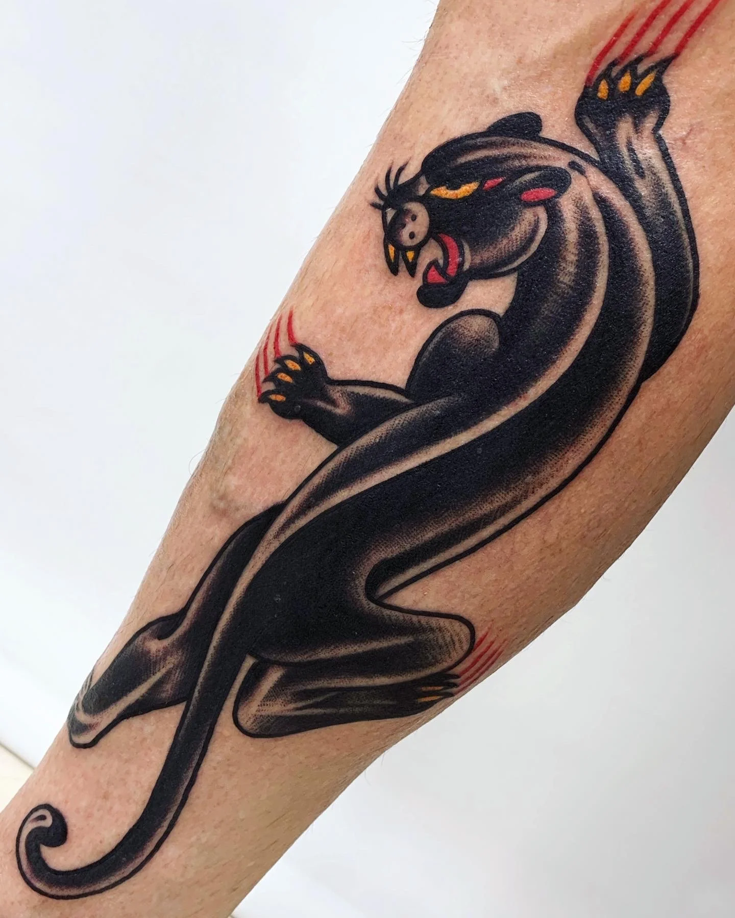 Tattoo of a black panther with yellow eyes and sharp teeth, showing its claws and snarling, on a person's arm.