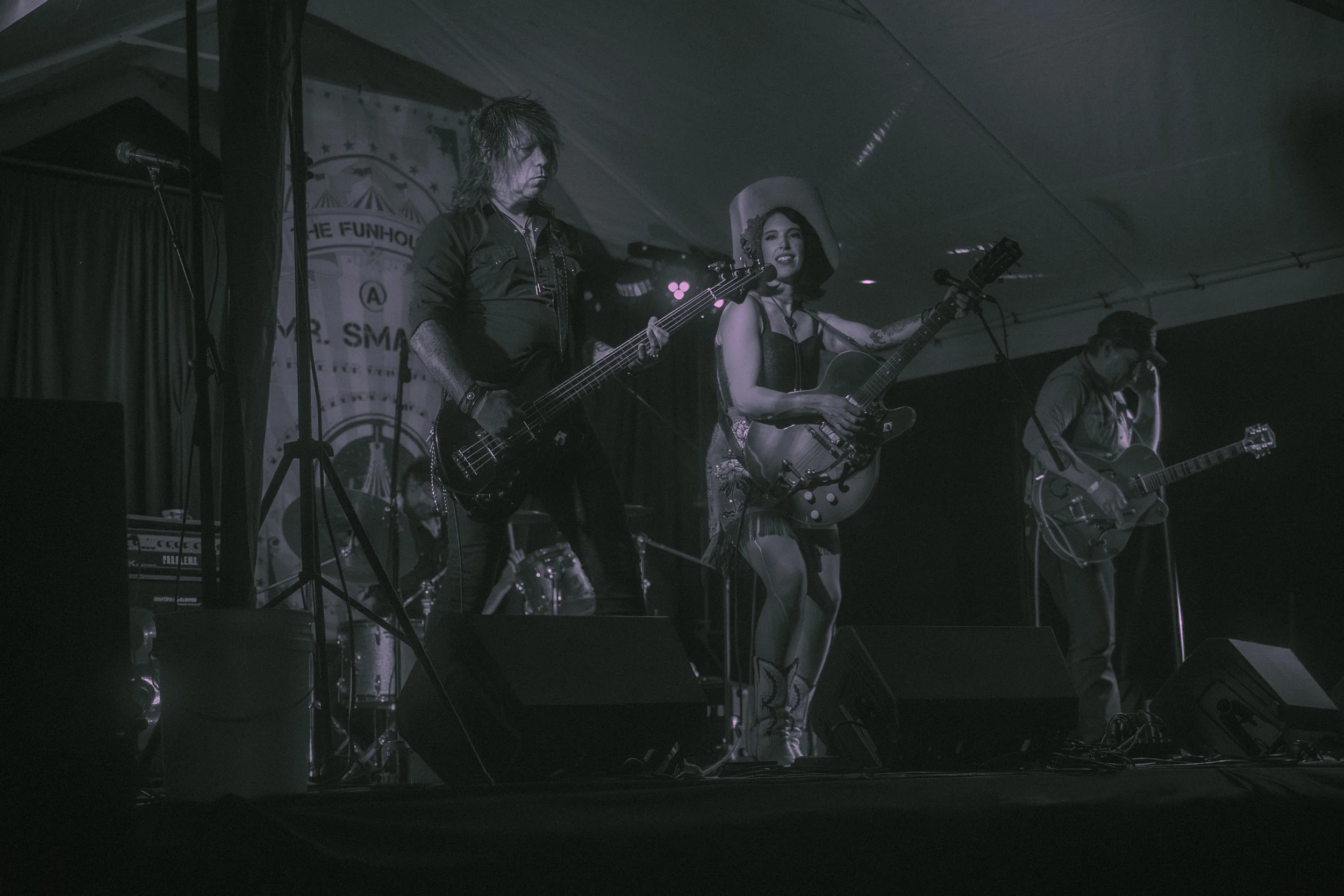 A band performing on stage, with members playing guitars and a female singer holding an acoustic guitar. WORK BY DAVEY