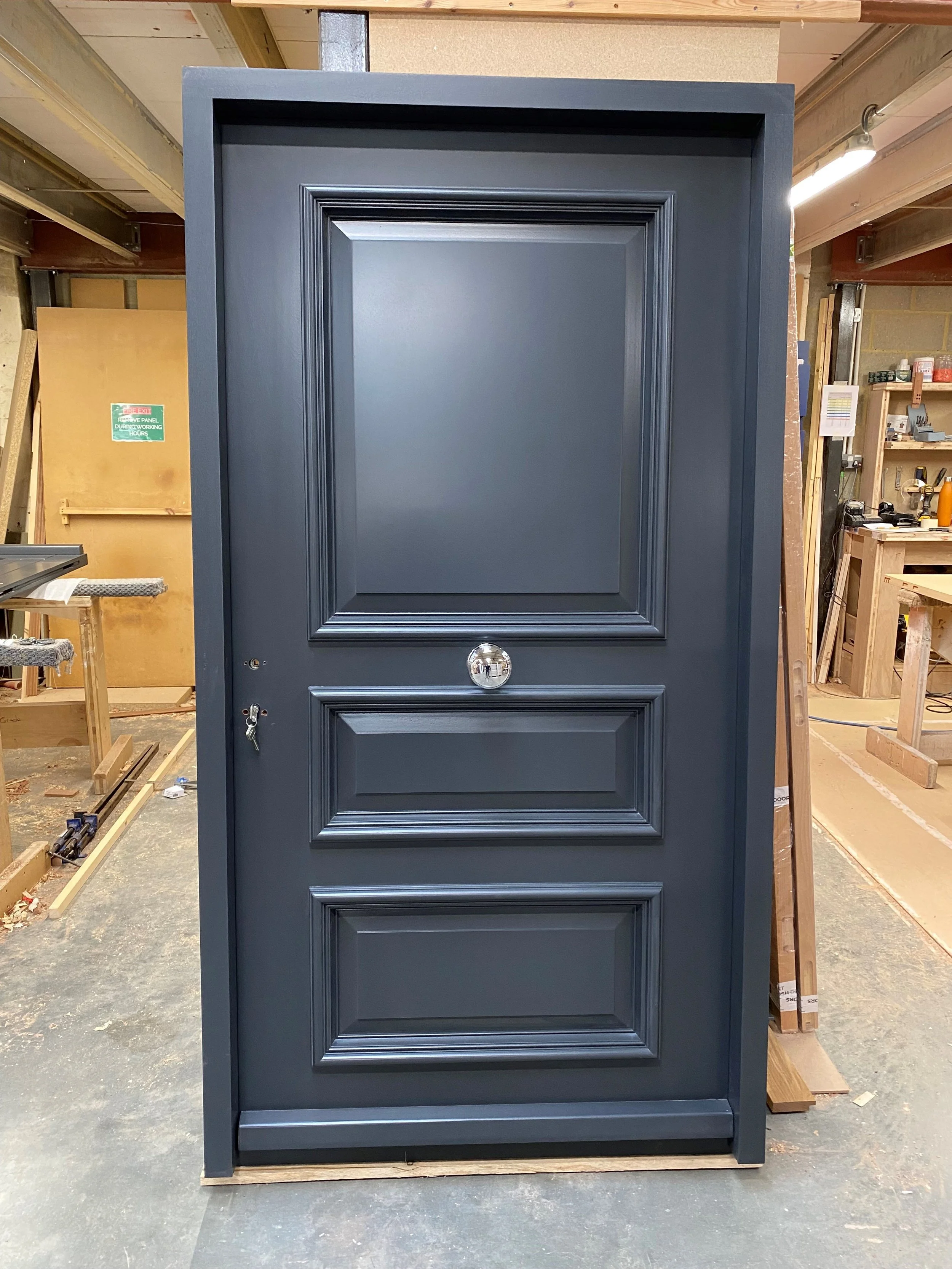 Dark blue front door with three panels, one large and two smaller, in a woodworking shop.