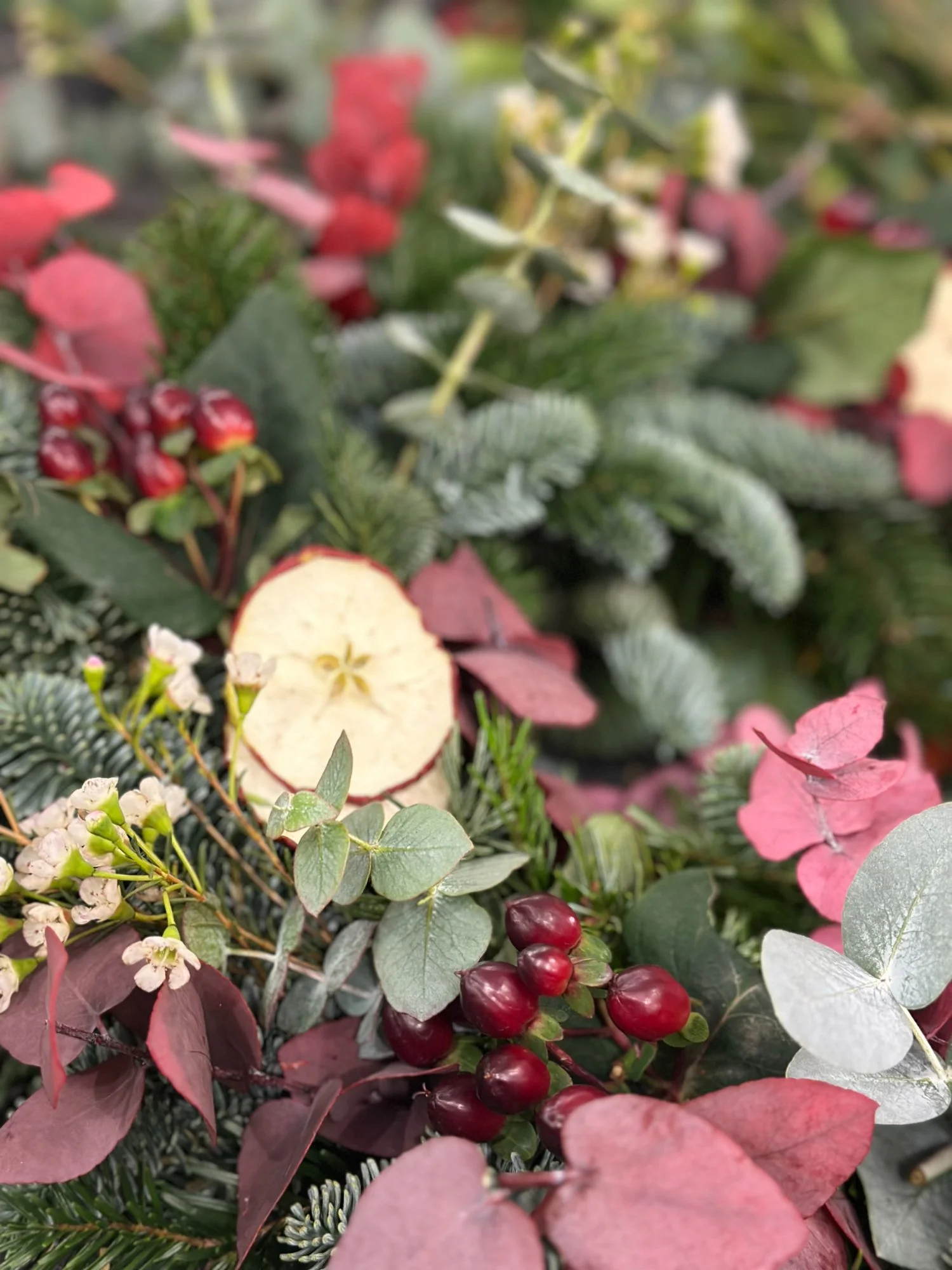 Close-up of natural Christmas wreath foliage featuring dried apple, red berries, eucalyptus and seasonal greenery at a Stems at 24 wreath-making workshop.