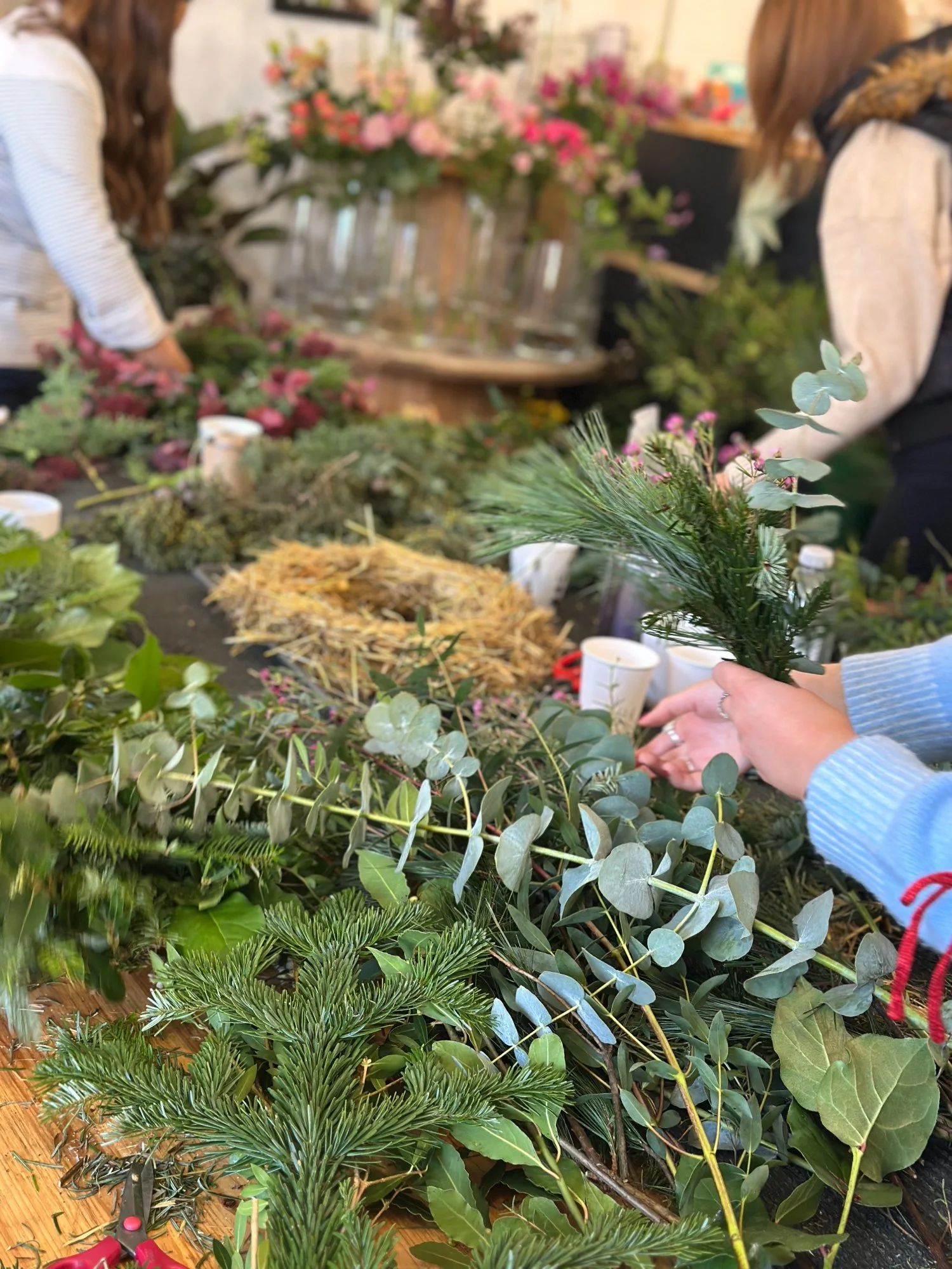 Guests selecting and arranging fresh winter foliage around a table during a natural Christmas wreath-making workshop at Stems at 24.