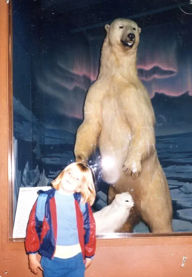 Child standing in front of a museum display featuring a life-sized polar bear and cub.