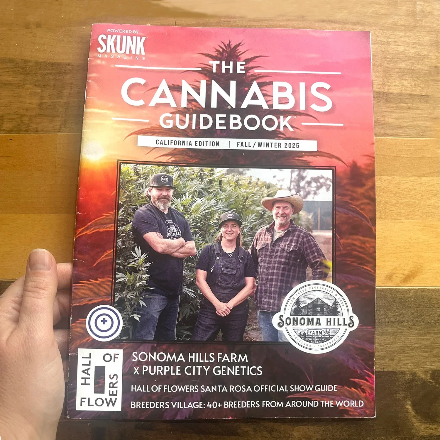 Cover of The Cannabis Guidebook, California edition, fall/winter 2025, featuring a photo of three people standing in a cannabis farm, with a sunset and trees in the background, and various text about the farm, genetics, and a show guide.