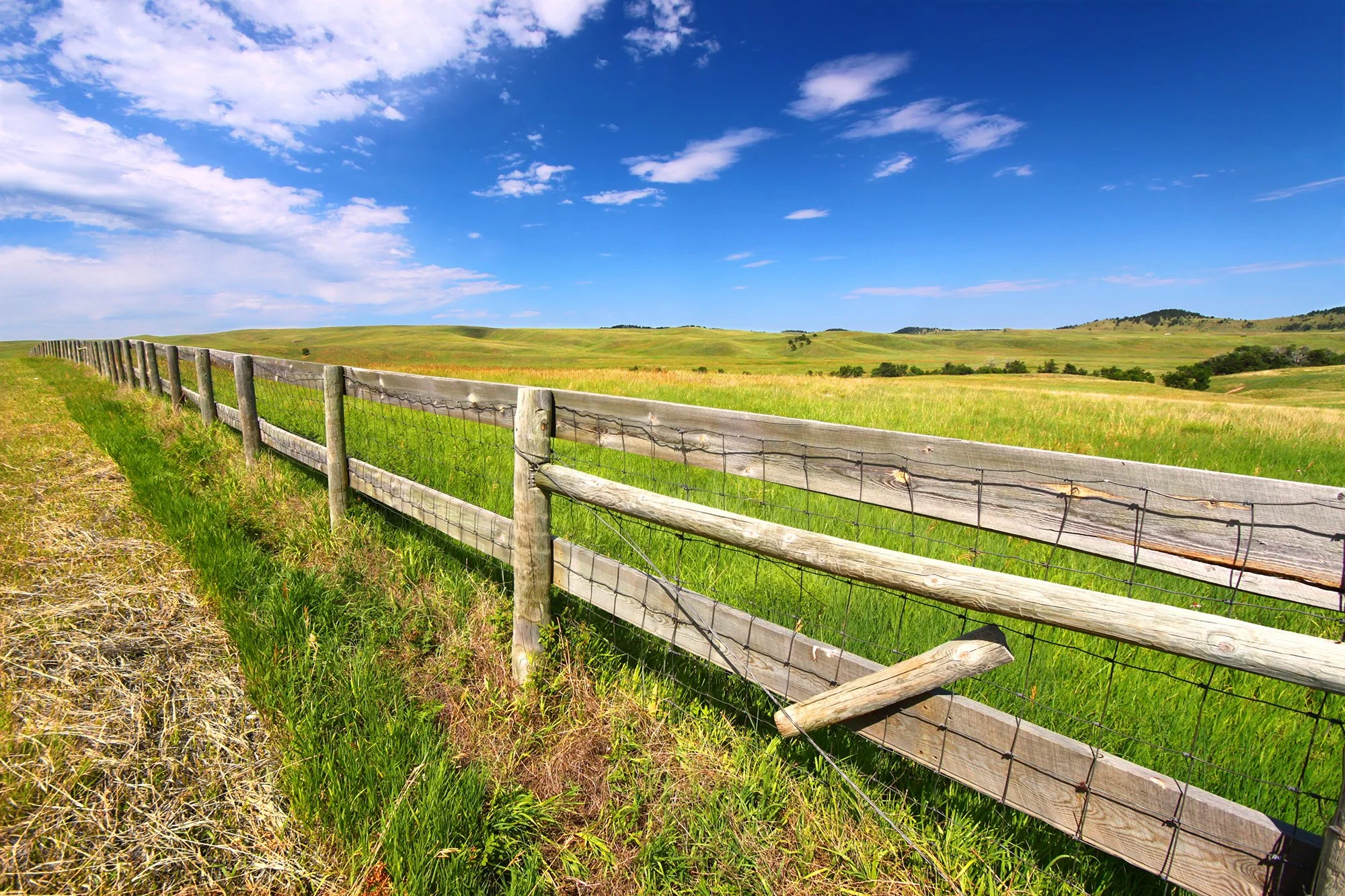 A field with a wooden fence with a blue sky and clouds.