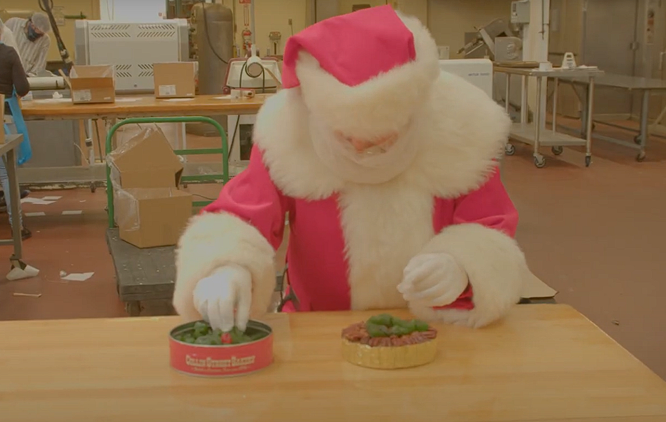 Person in a Santa Claus costume preparing food on a work table in a factory or kitchen environment.