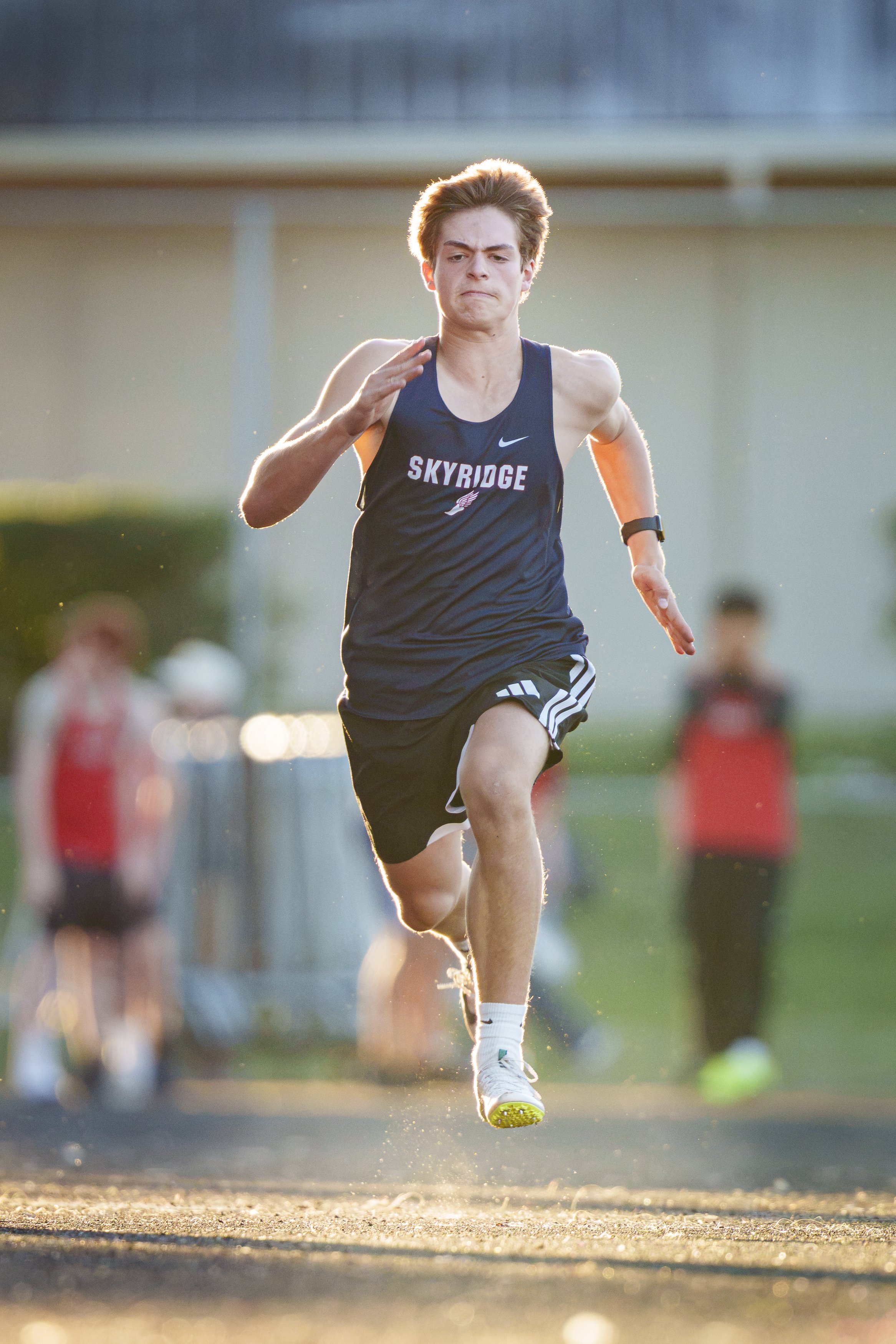 A middle school male track athlete is in mid-stride in the 100 meter race.