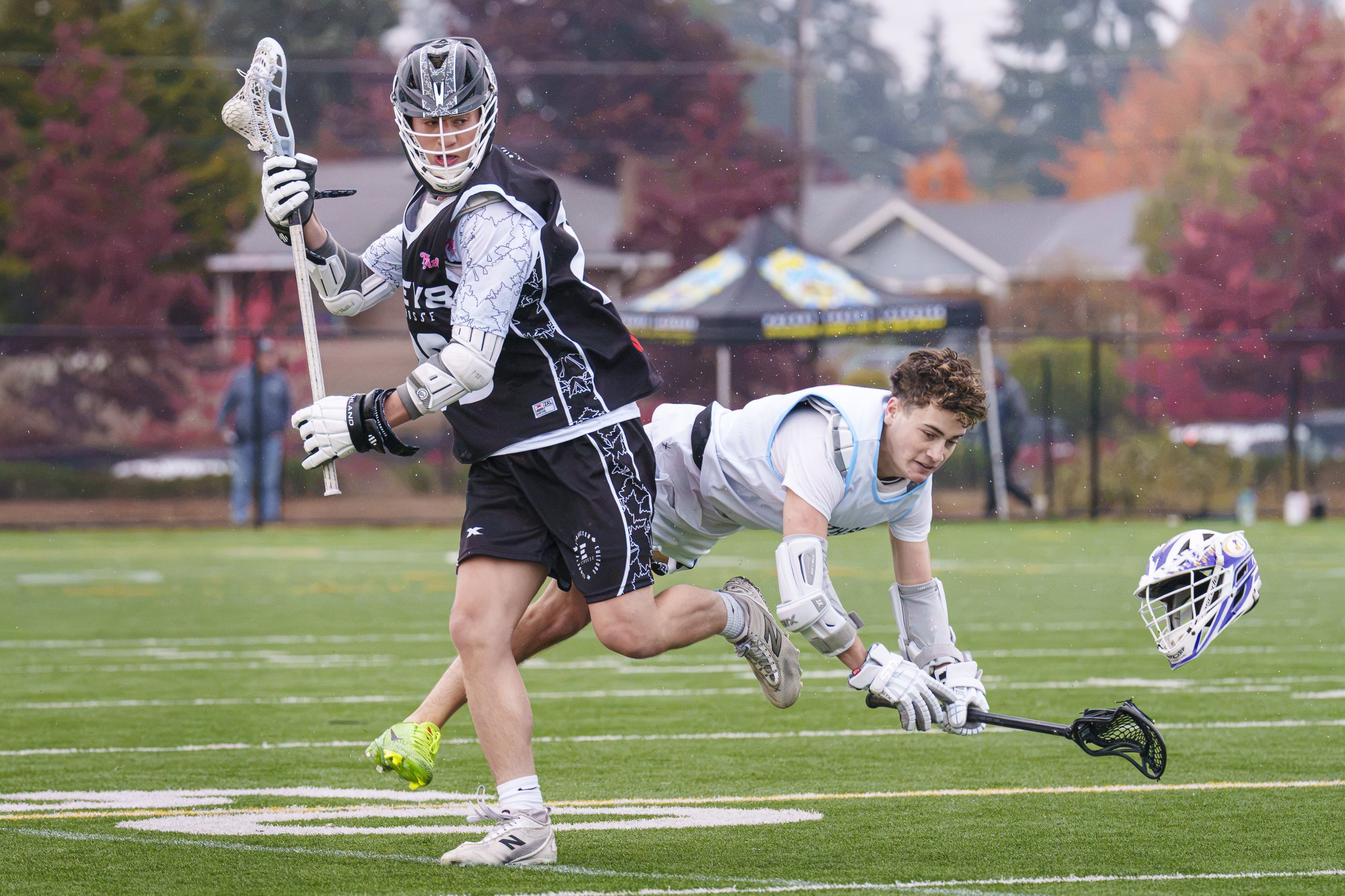 Two high school lacrosse players in tournament play.  One player has just completed a check while the other is falling toward the ground, his helmet in mid-air as he falls.